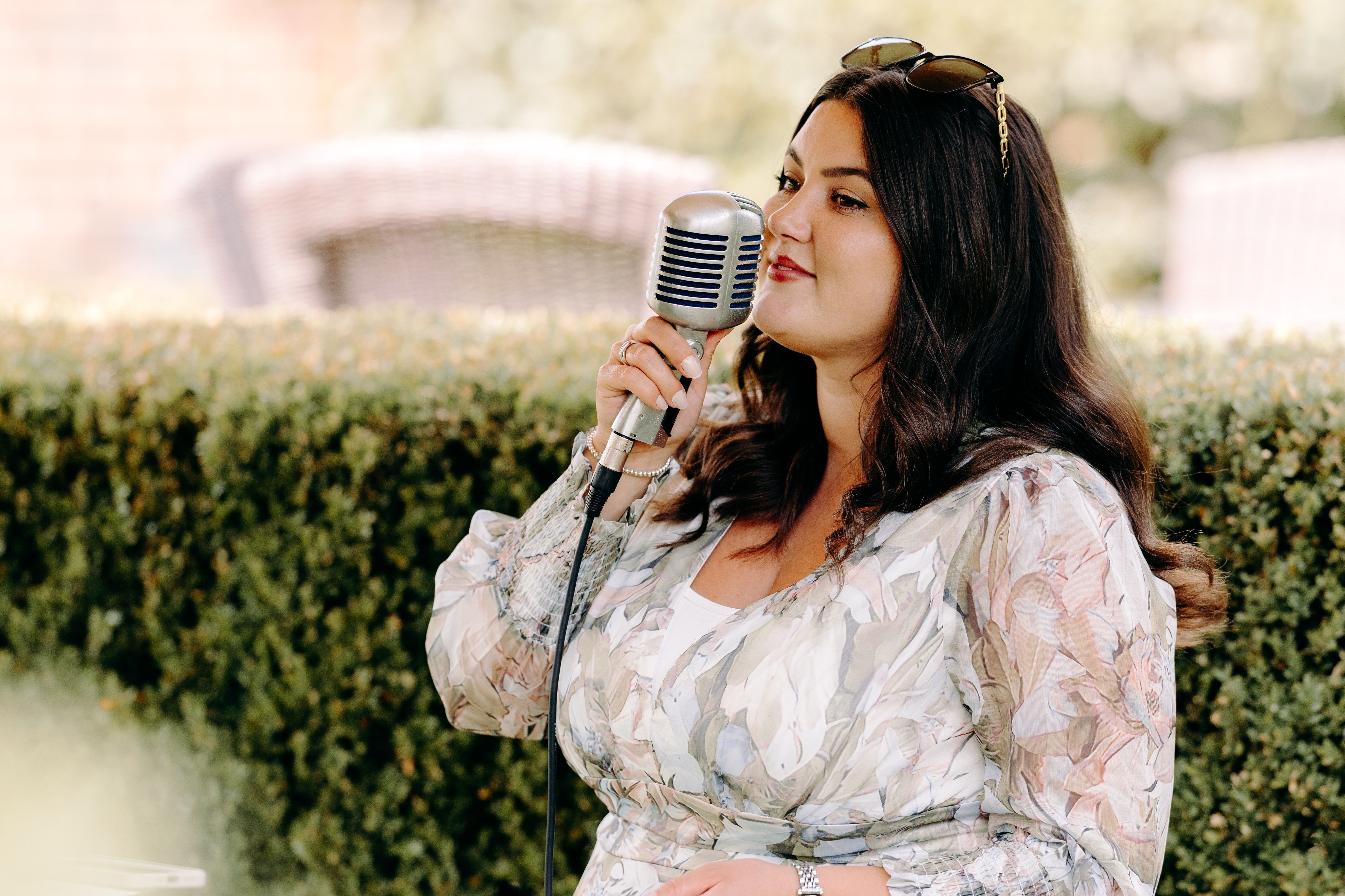 Woman in a floral dress singing into a vintage microphone outdoors