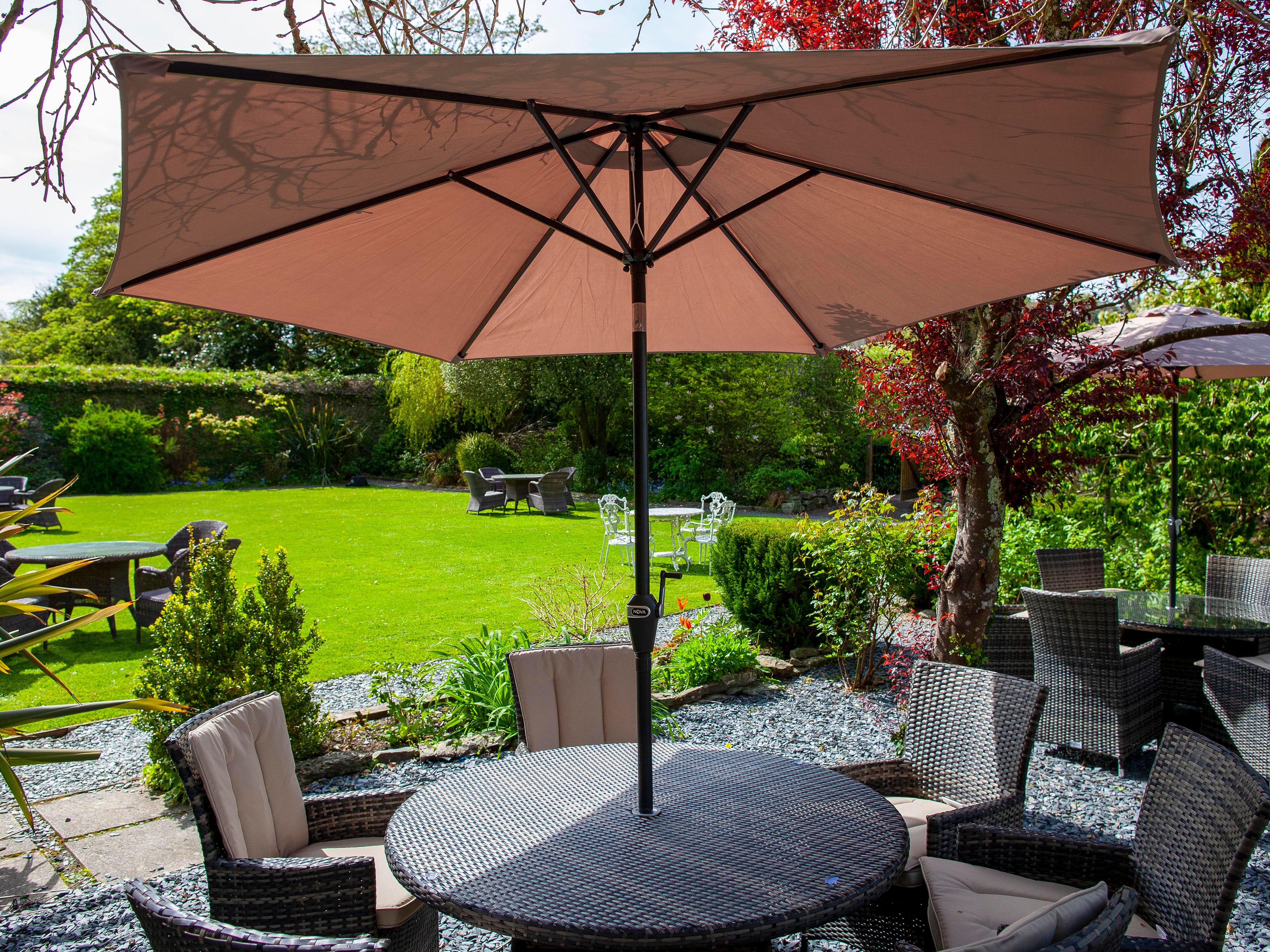 Outdoor patio area with wicker furniture and a large umbrella shade in a garden setting