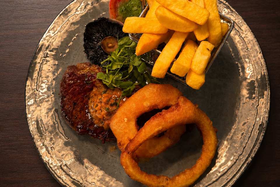 A plate with steak, onion rings, French fries, grilled tomato, mushroom, and greens.