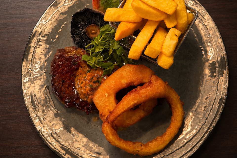 A plate with steak, onion rings, French fries, grilled tomato, mushroom, and greens.