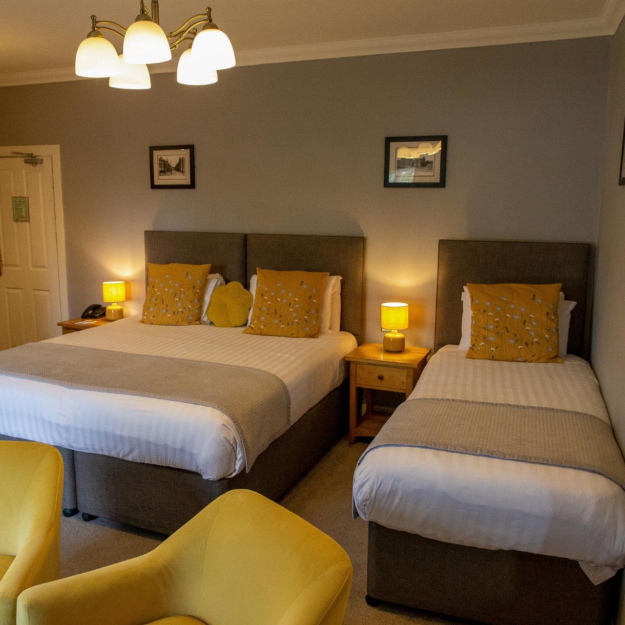 Family hotel room with one double bed, one single bed, yellow pillows, and yellow chairs