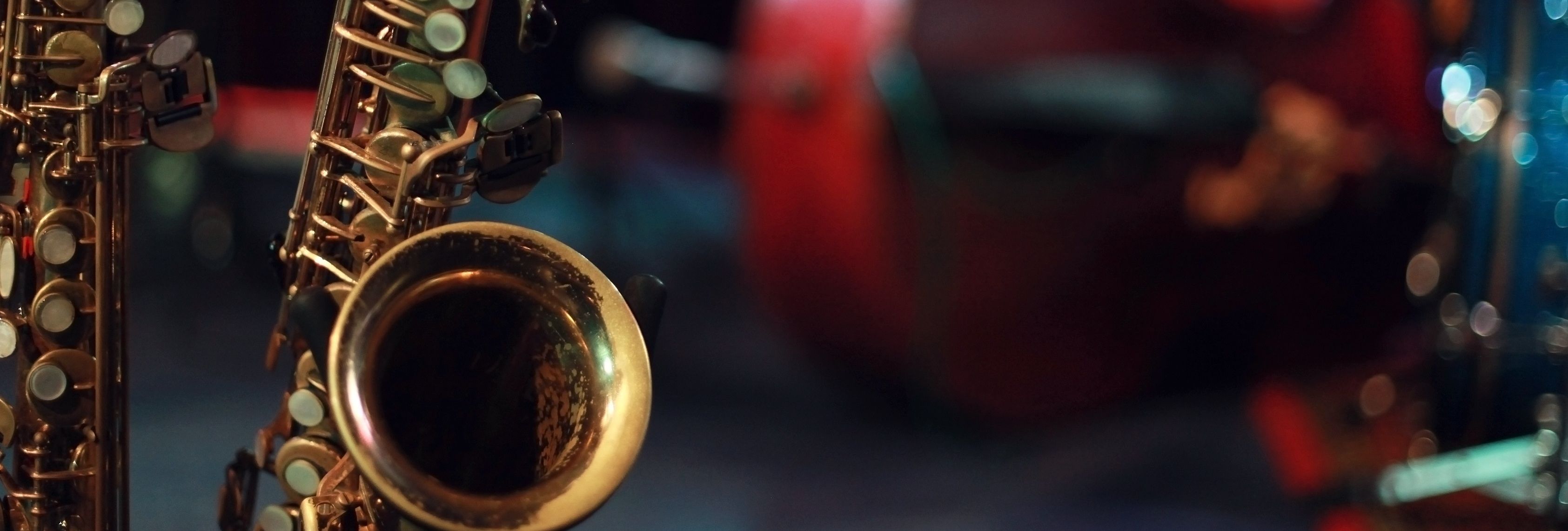 Close-up of saxophones on a dimly lit stage with blurred red chair and drum kit in the background