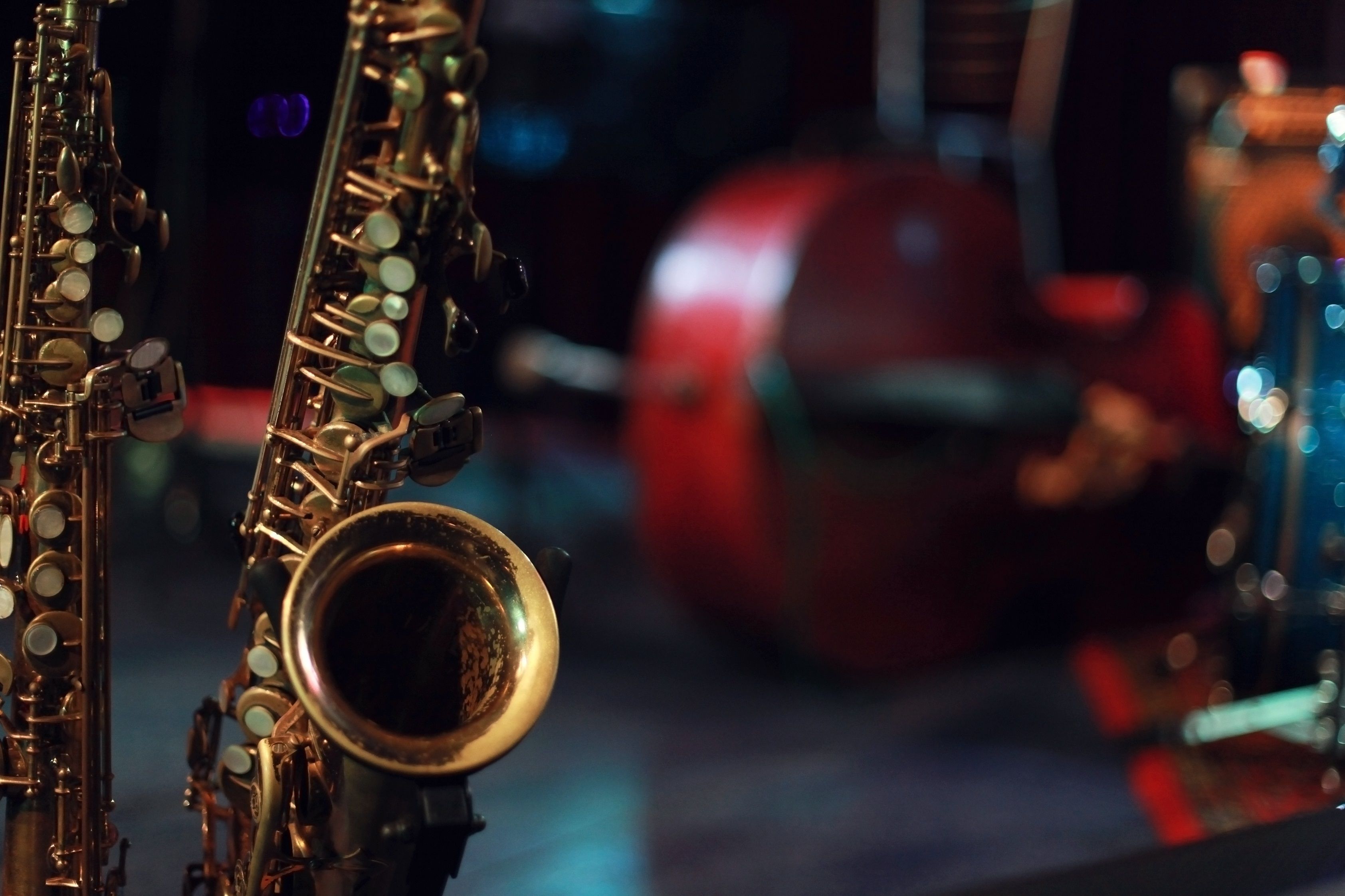 Close-up of saxophones on a dimly lit stage with blurred red chair and drum kit in the background