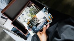 A person holding old printed photos above an open box filled with euro banknotes and more photographs.