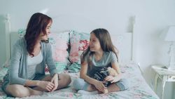 Woman and young girl sitting on a bed and smiling at each other