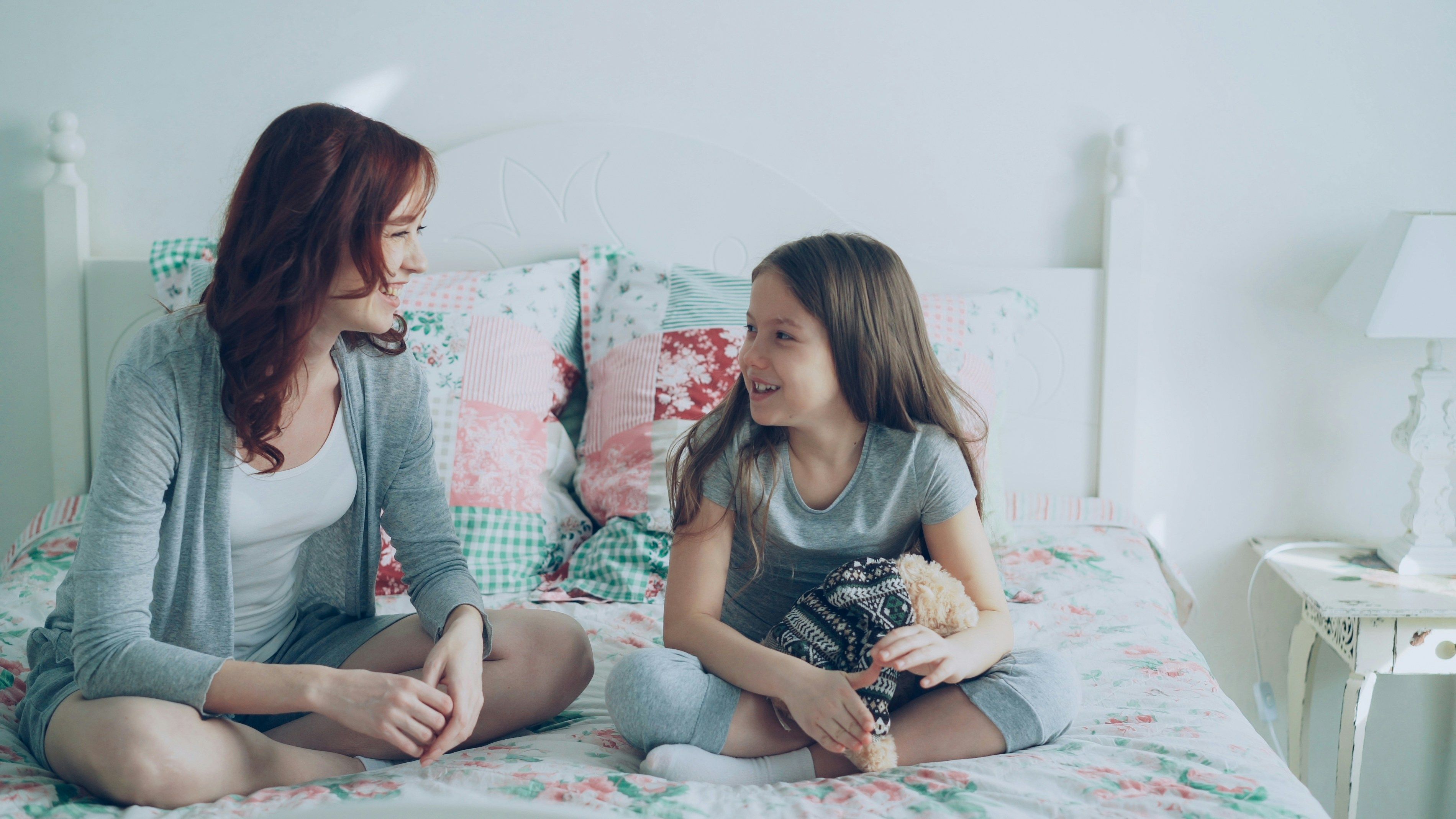 Woman and young girl sitting on a bed and smiling at each other