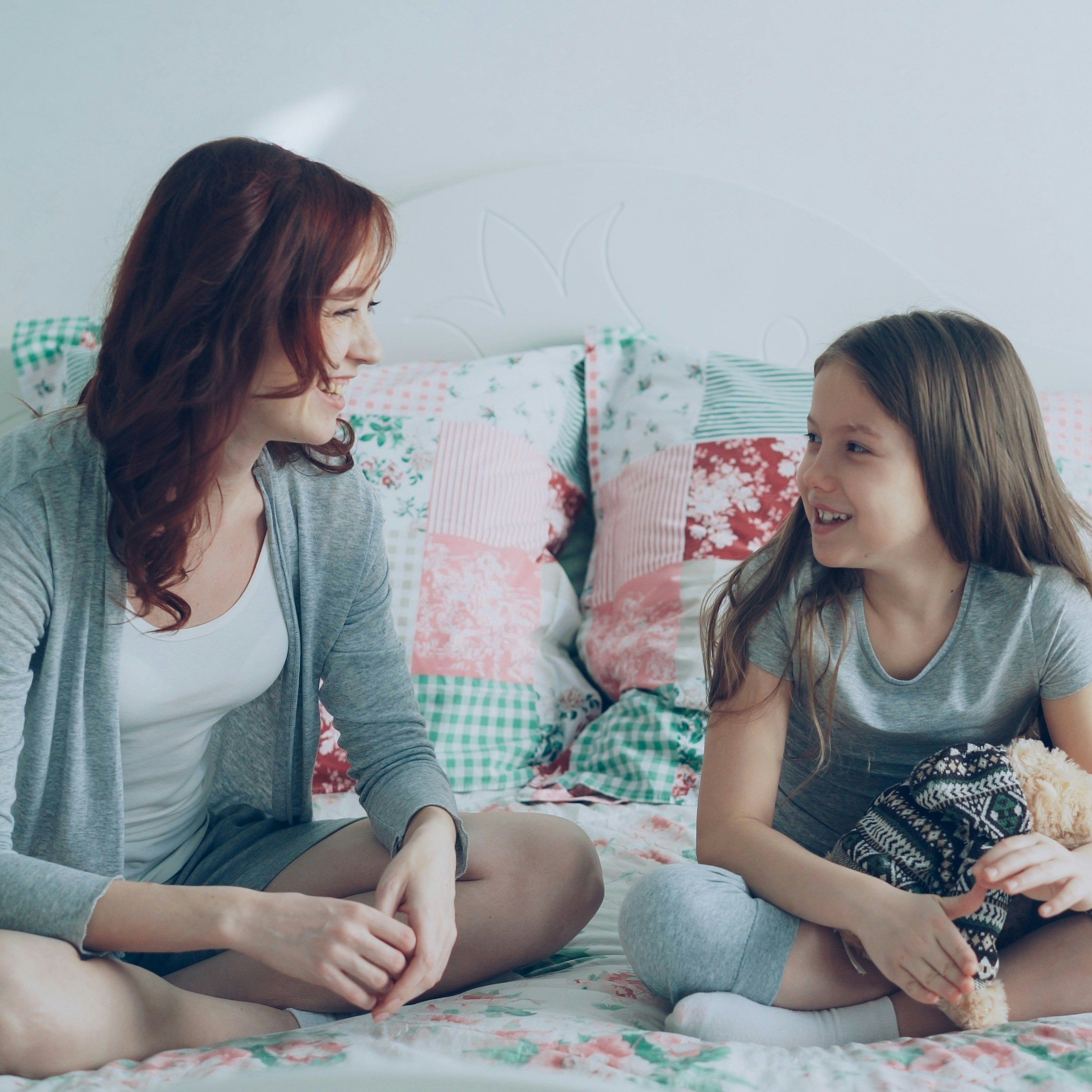 Woman and young girl sitting on a bed and smiling at each other
