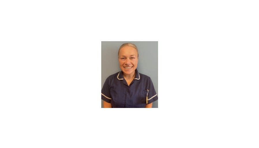 Smiling woman in a navy blue nurse uniform standing against a light blue background