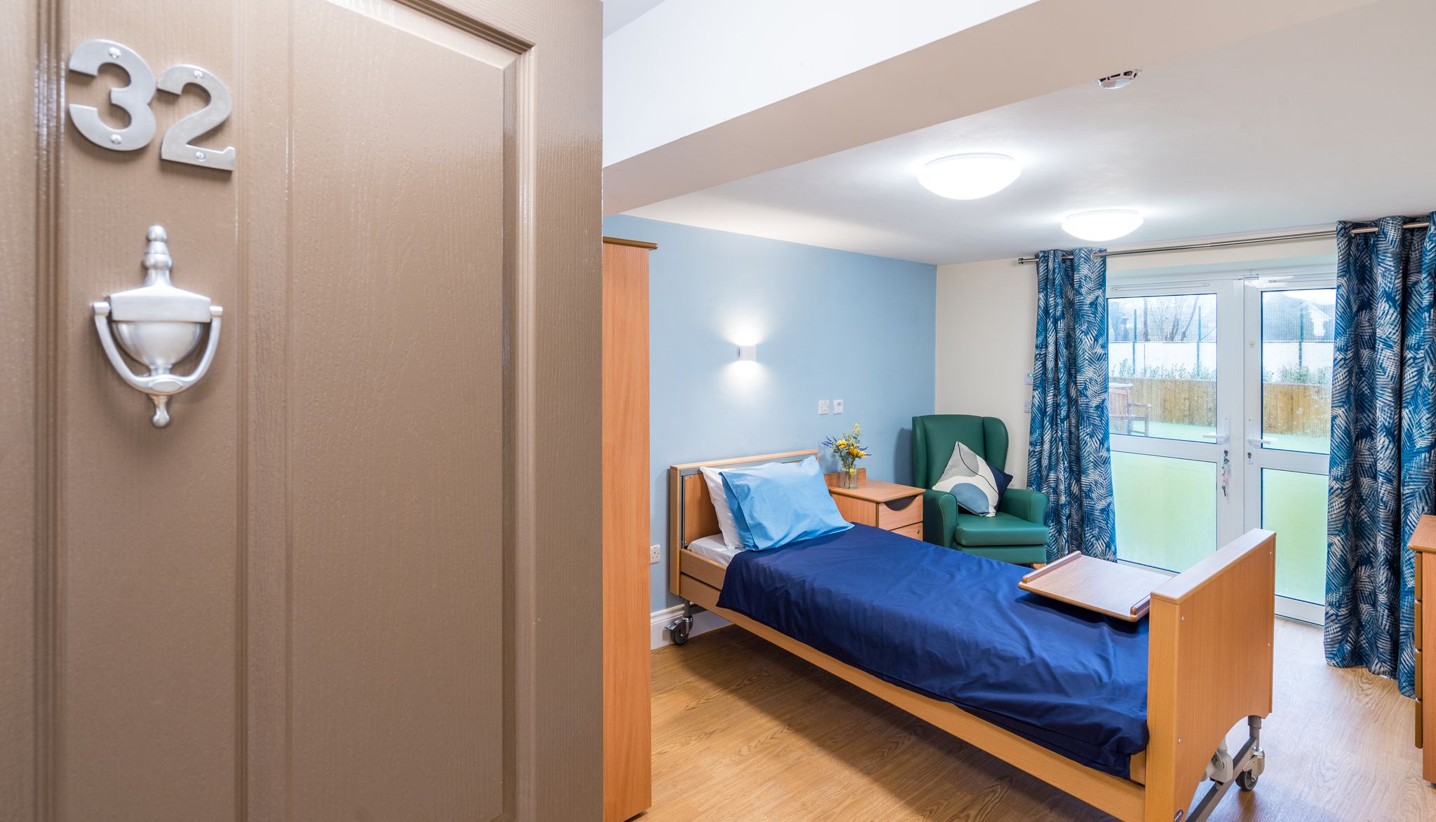 Bedroom with blue bedding and large window with view over garden
