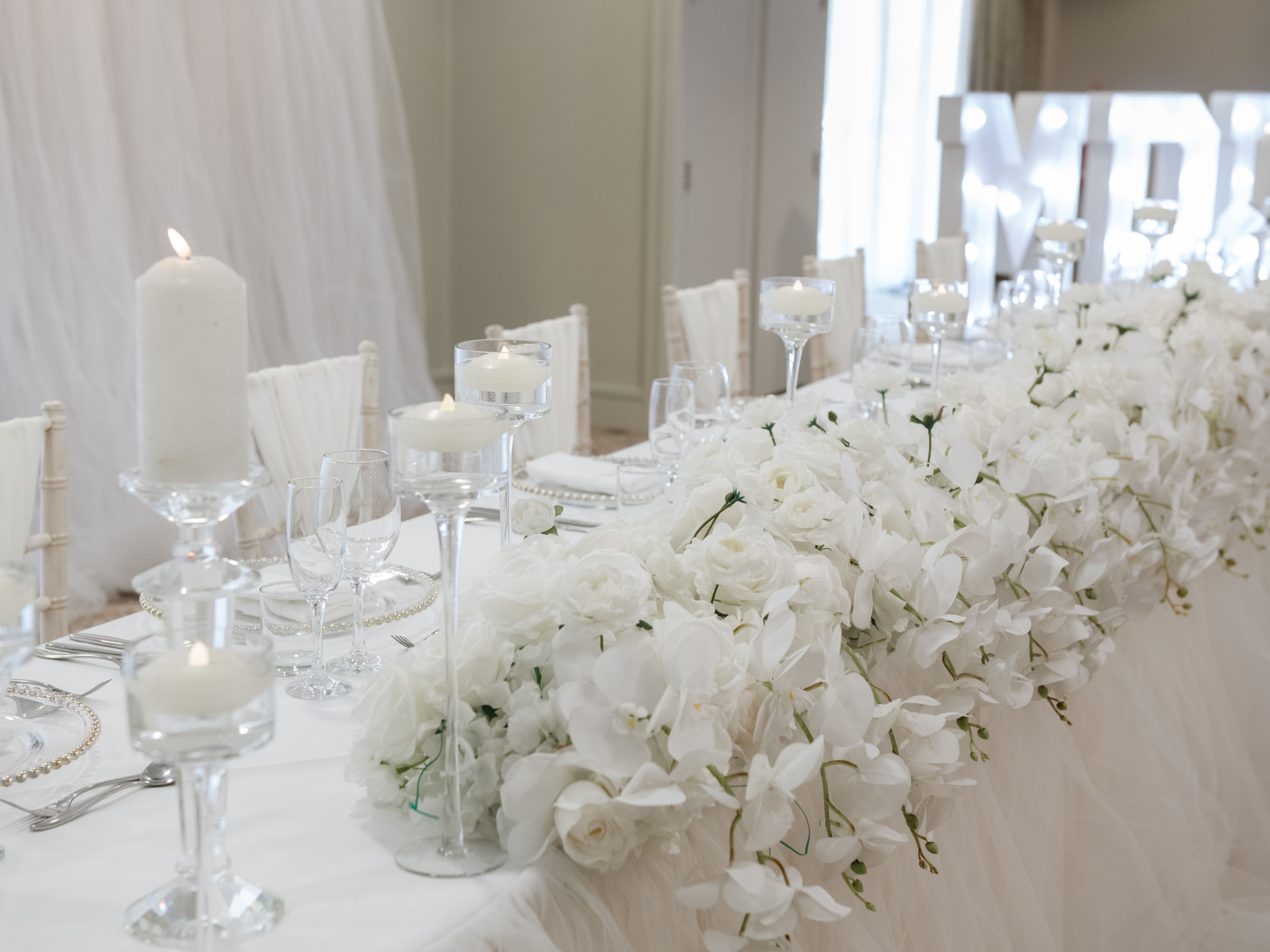 Elegant wedding reception table decorated with white flowers, candles, and crystal glassware.