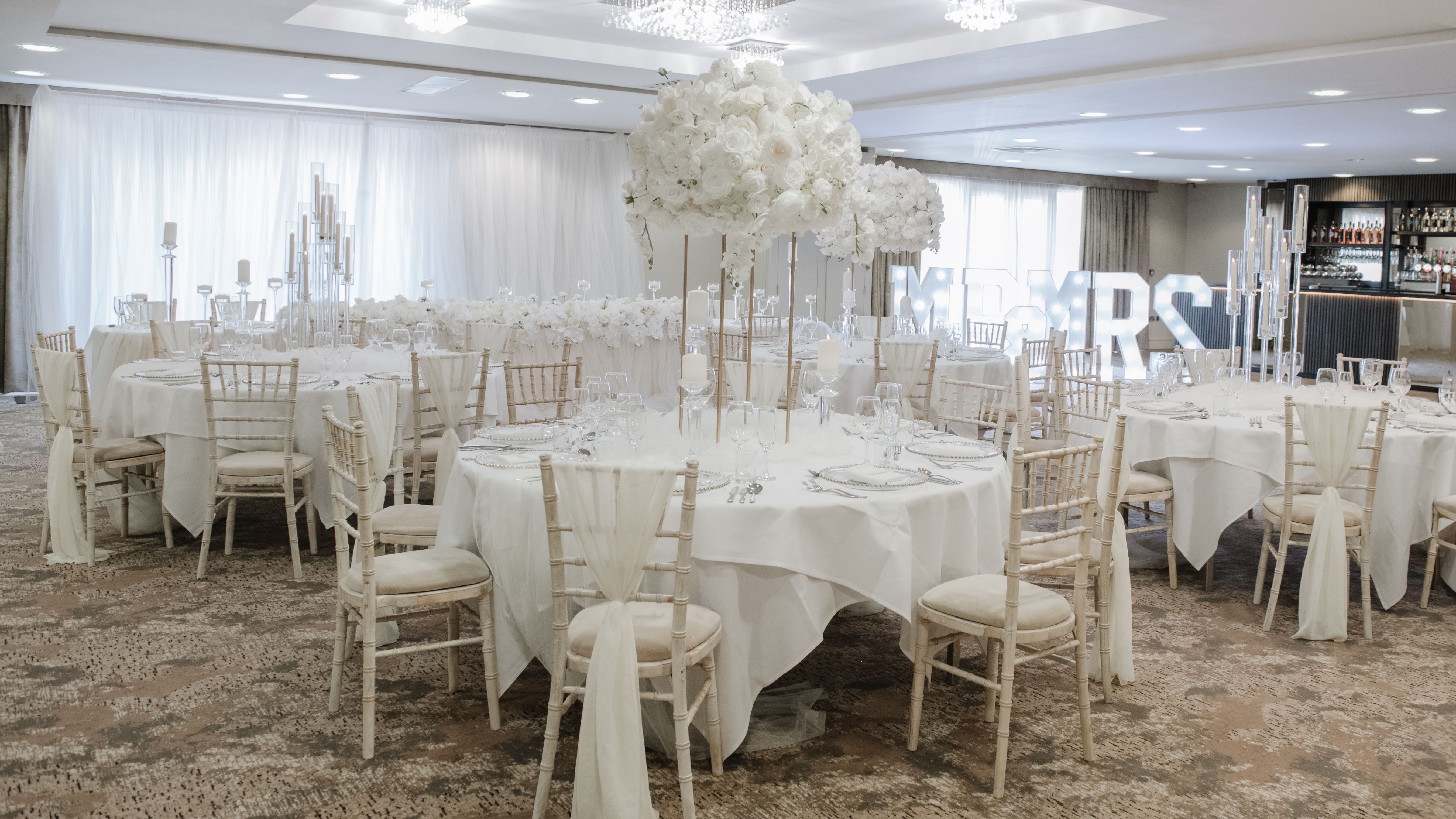 Elegant wedding reception setup with white floral centerpieces and white draped chairs