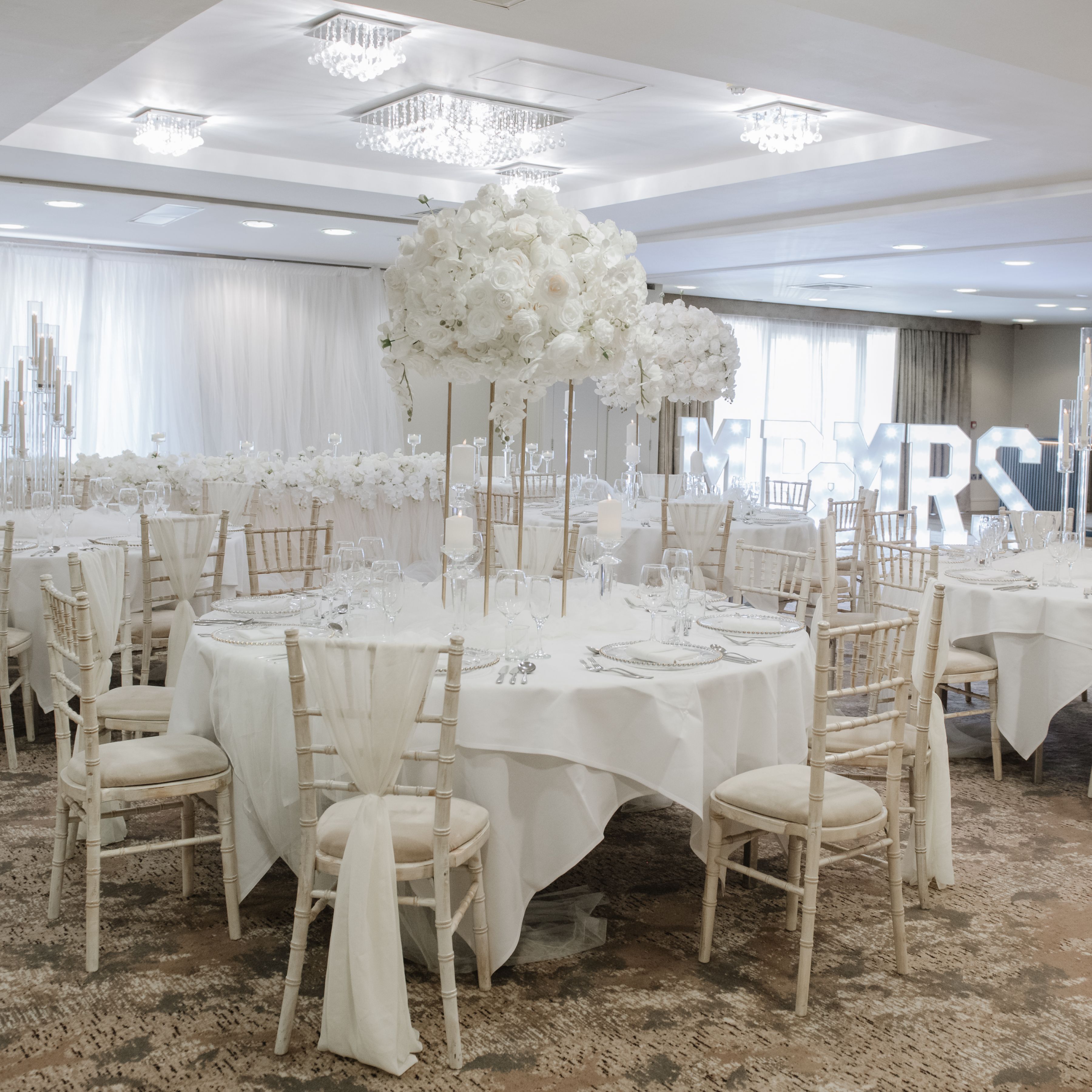 Elegant wedding reception setup with white floral centerpieces and white draped chairs
