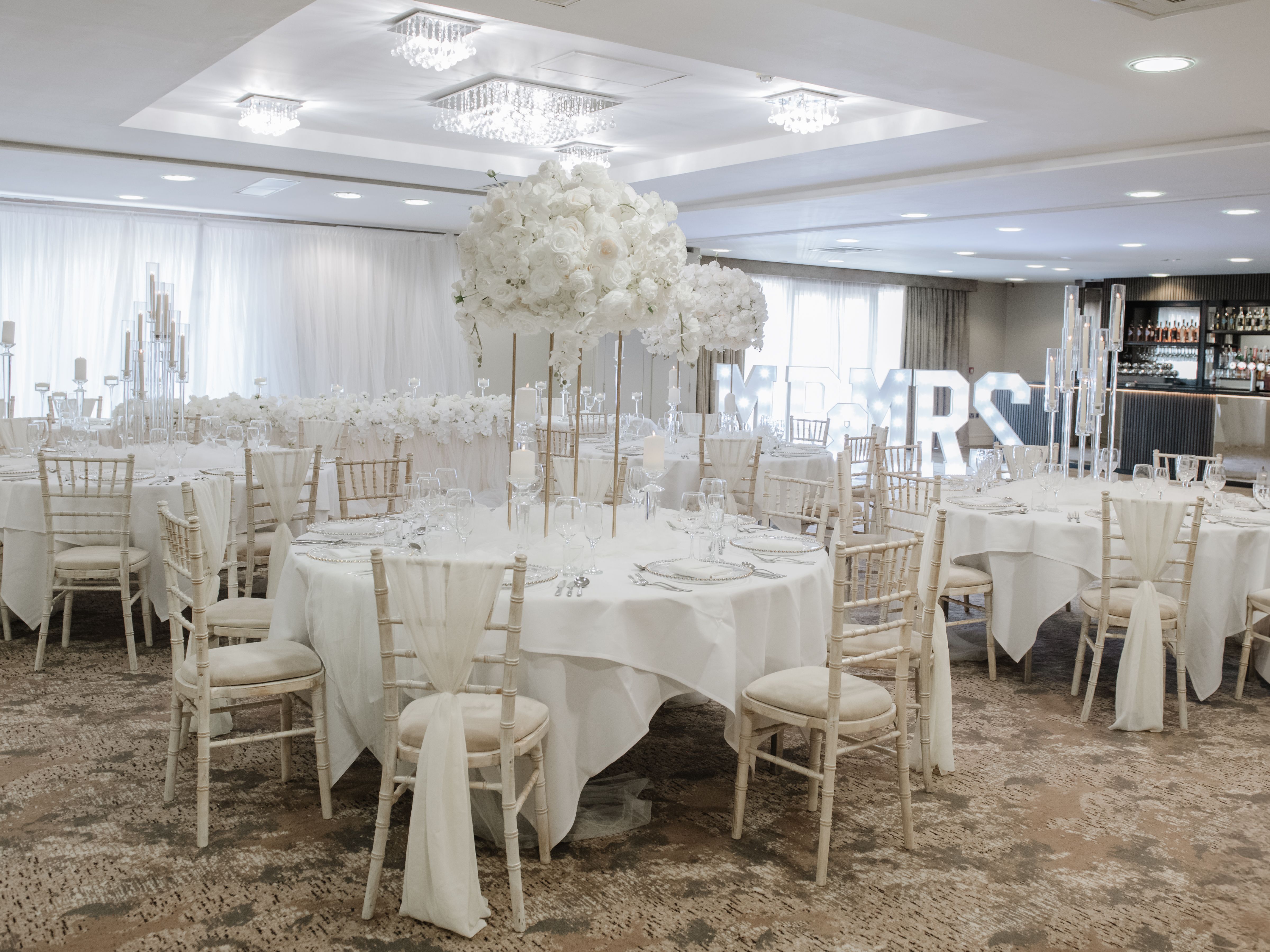 Elegant wedding reception setup with white floral centerpieces and white draped chairs