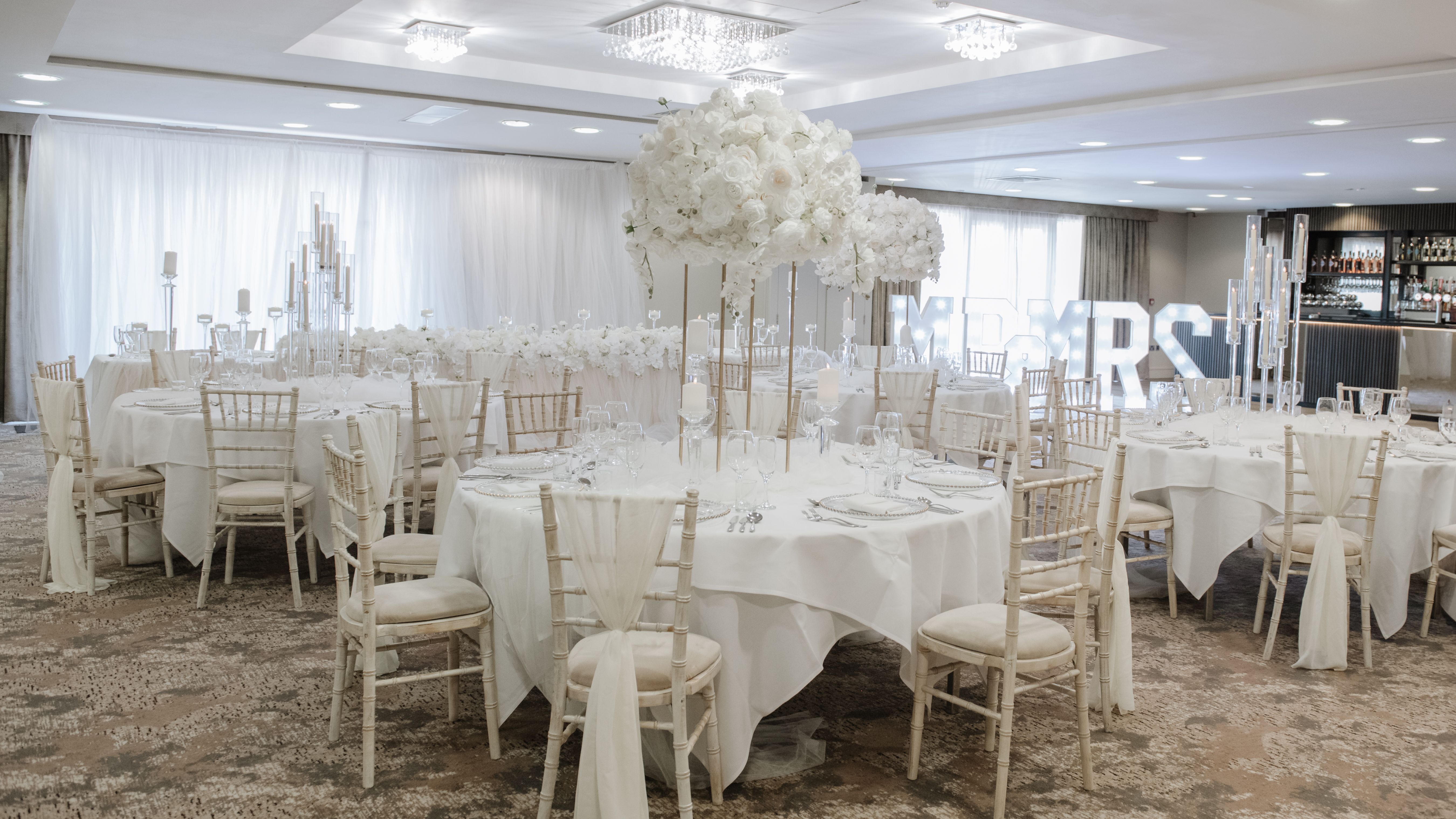 Elegant wedding reception setup with white floral centerpieces and white draped chairs