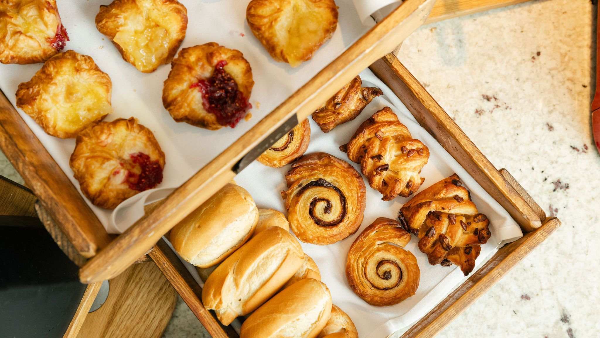 Assorted pastries and bread rolls in wooden trays on a countertop