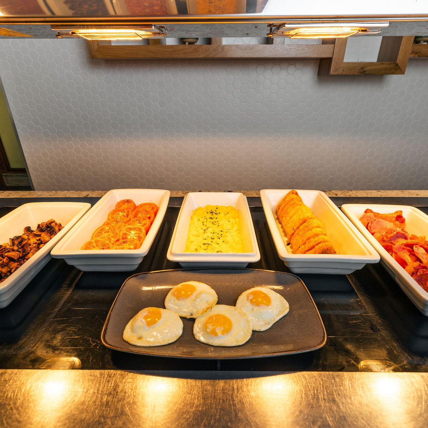 Breakfast buffet with eggs, bacon, tomatoes, mushrooms, hash browns, beans, and sausages