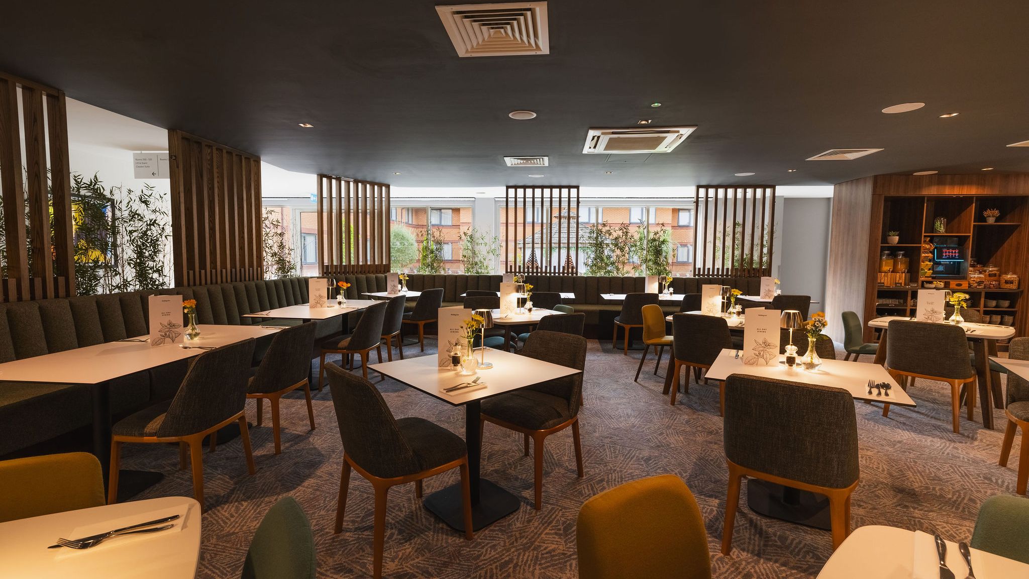 Modern hotel restaurant with neatly arranged tables and chairs, soft lighting, and decor featuring green plants.