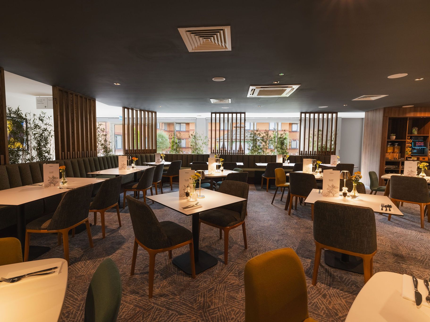 Modern hotel restaurant with neatly arranged tables and chairs, soft lighting, and decor featuring green plants.