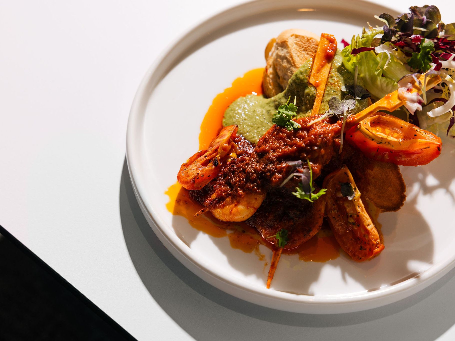Gourmet seafood dish with shrimp, sauce, vegetables, and greens on a white plate
