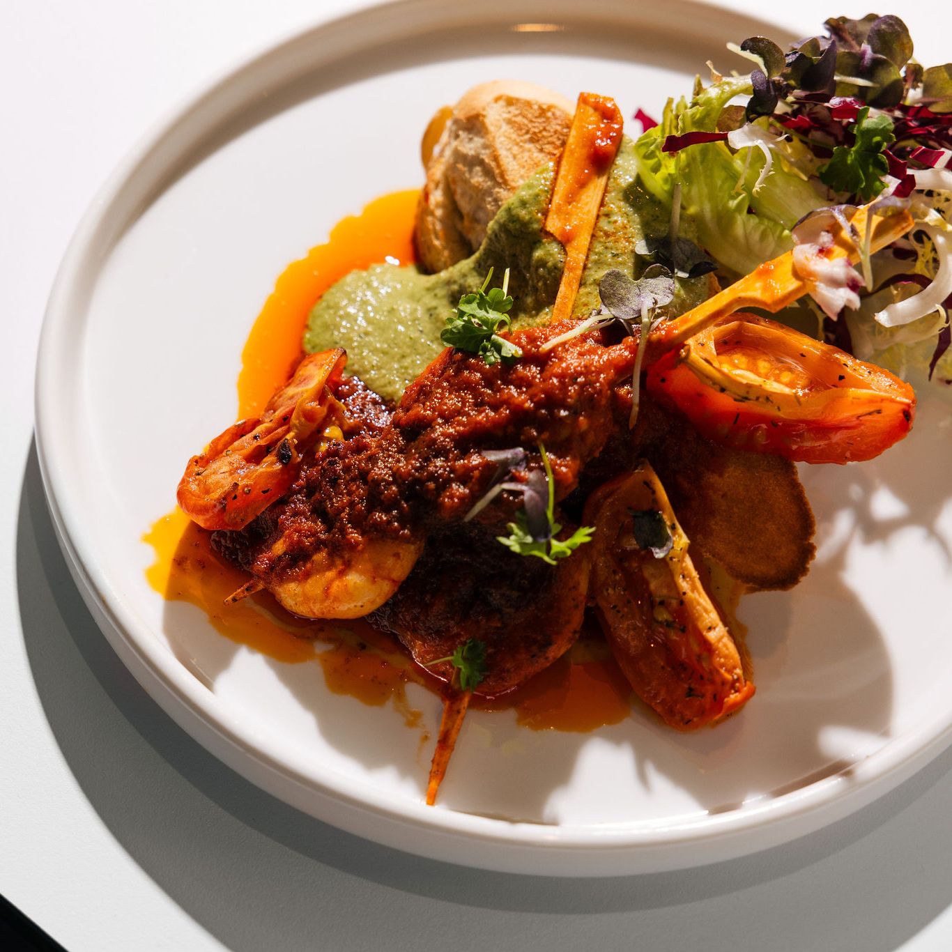 Gourmet seafood dish with shrimp, sauce, vegetables, and greens on a white plate
