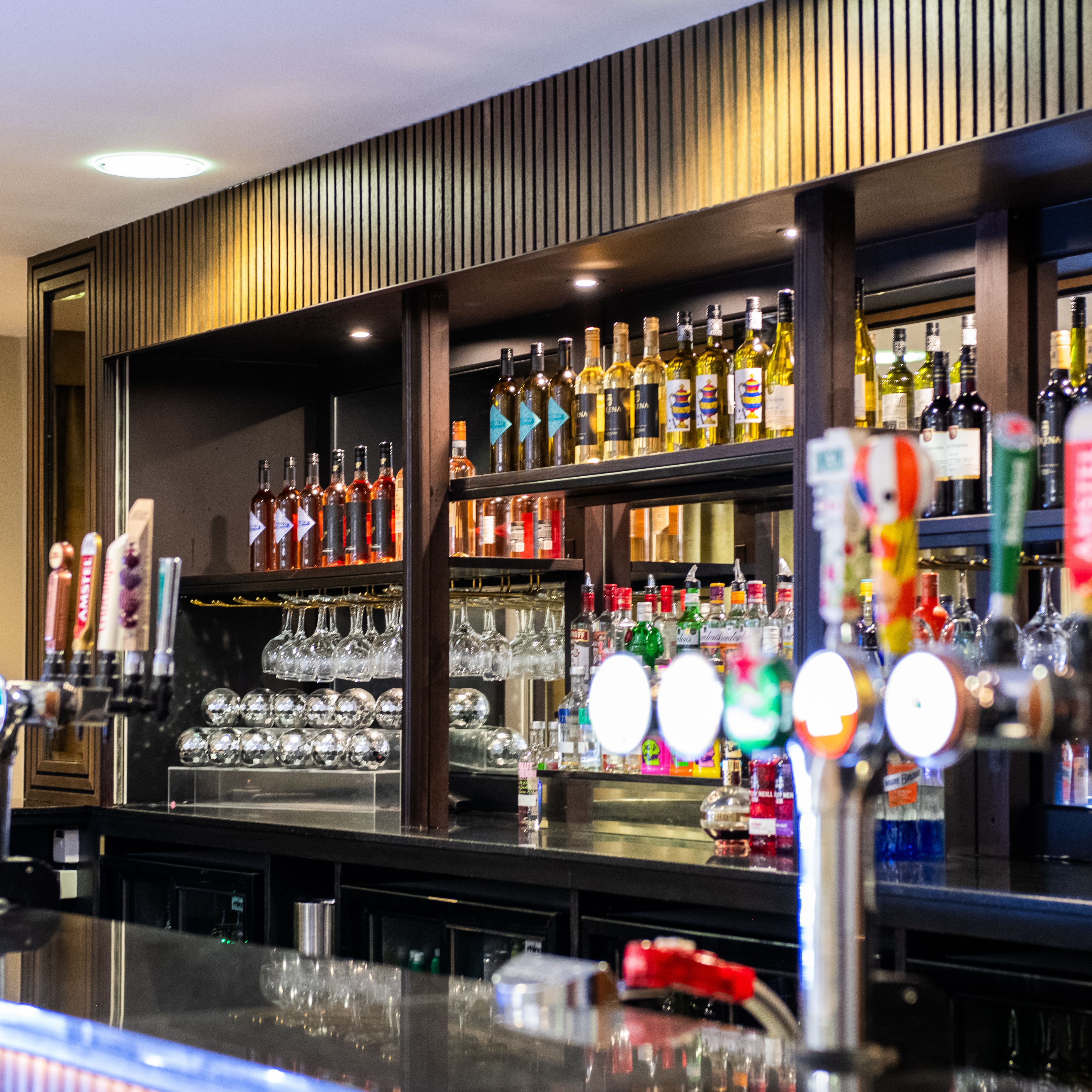 A bar counter with beer taps and shelves of bottles and glasses behind it.
