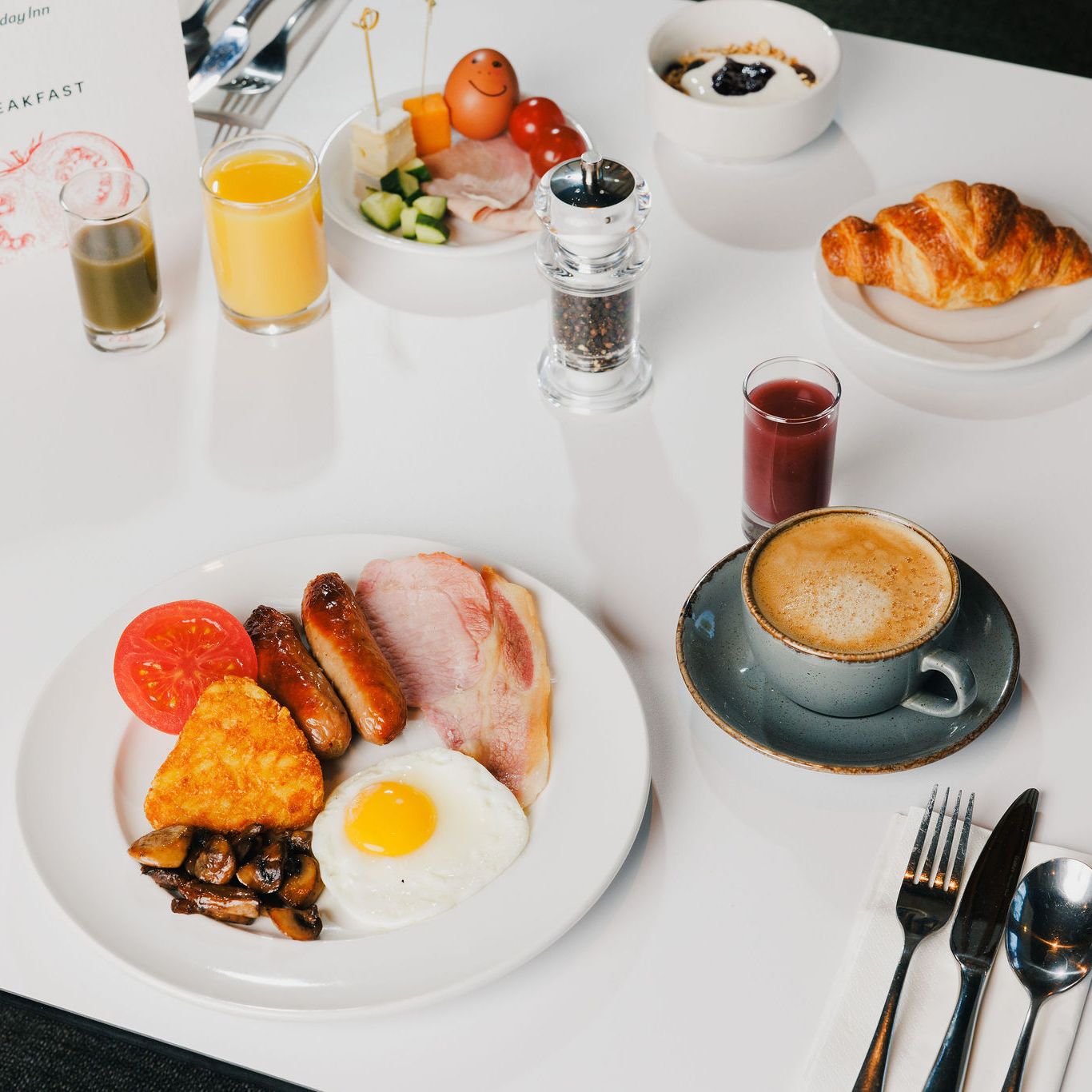Hotel breakfast spread with traditional English breakfast, juice, coffee, croissant, and fruit.