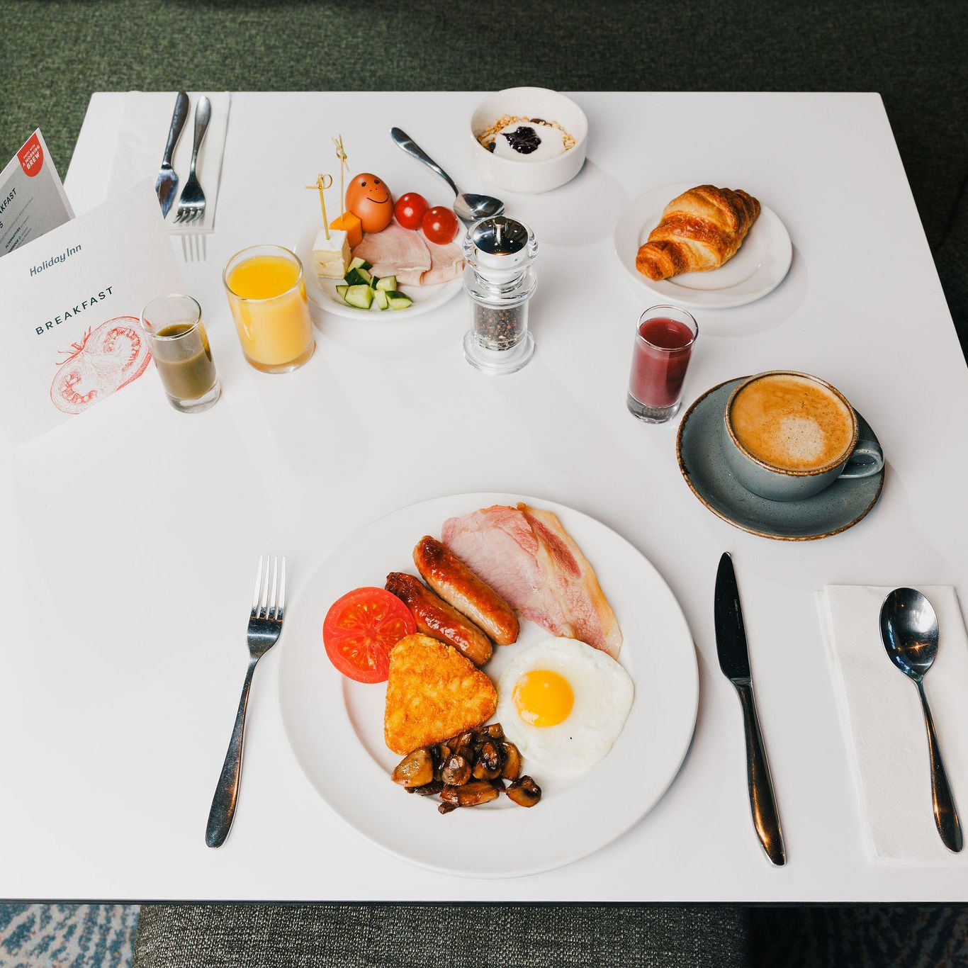 Holiday Inn breakfast table with full English breakfast, juice, coffee, croissant, and yogurt.