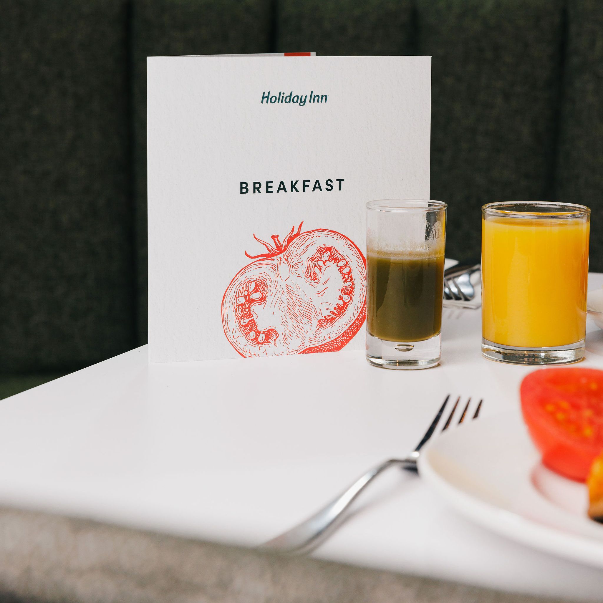 Holiday Inn breakfast menu on a table with two glasses of juice and a plate with tomato slice.