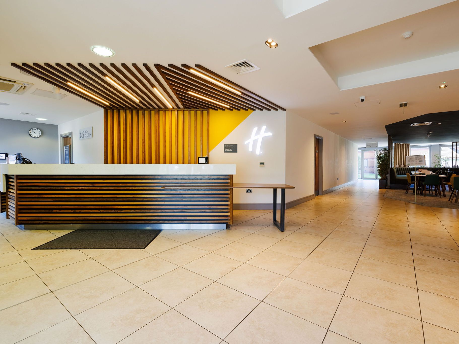 Modern hotel reception area with stylish wooden desk, yellow accent wall, and open seating area.