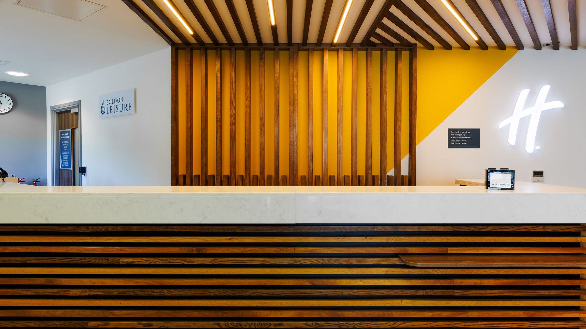 Modern hotel reception desk with wooden accents and a bright yellow feature wall