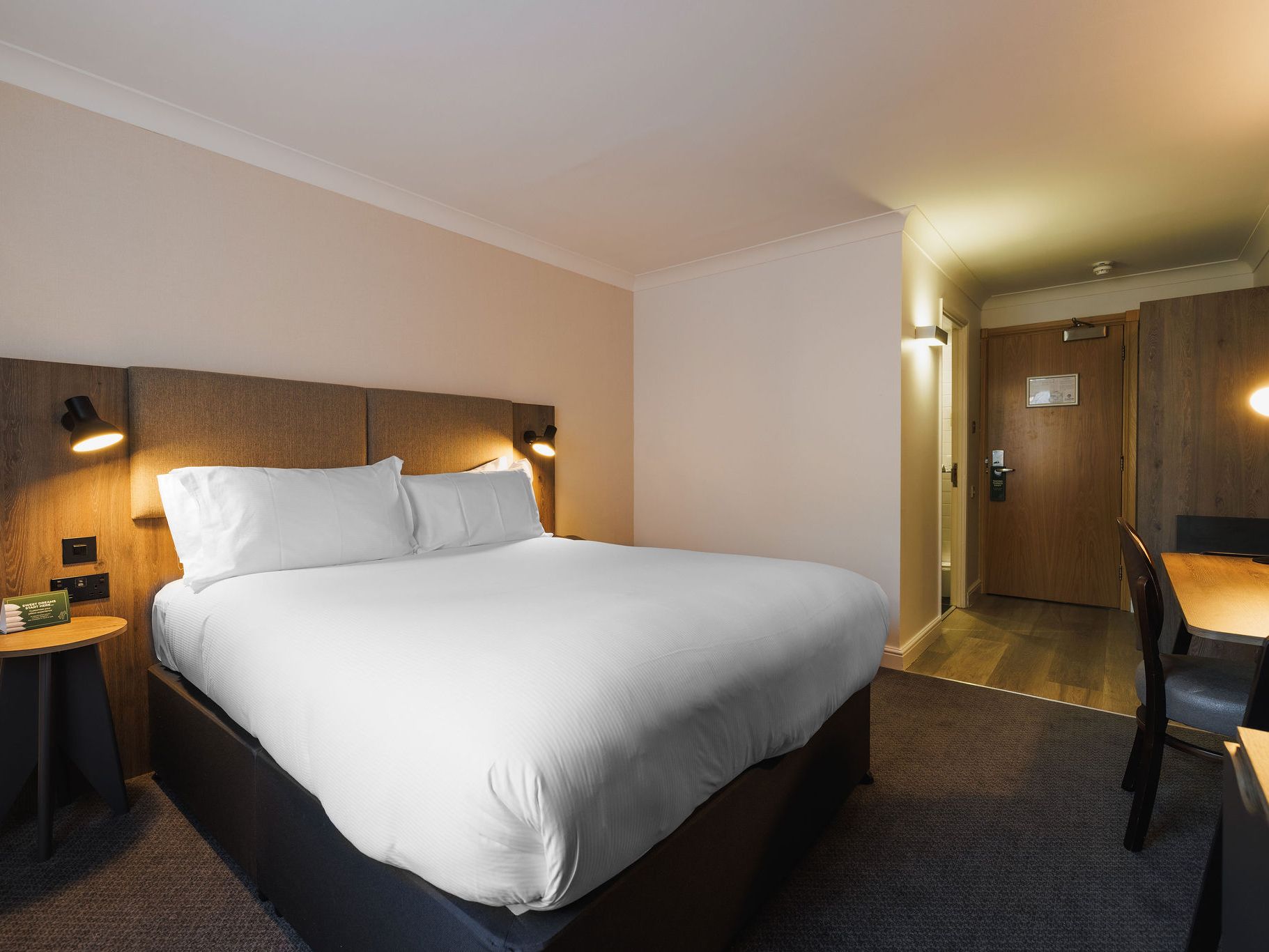 Modern hotel room with large bed, desk, and warm lighting