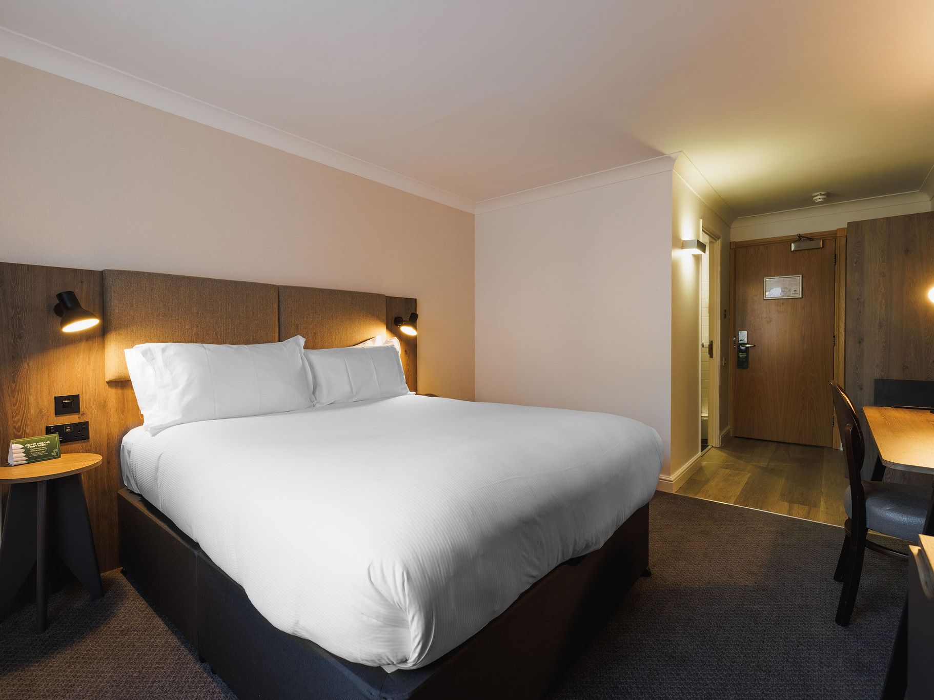 Modern hotel room with large bed, desk, and warm lighting