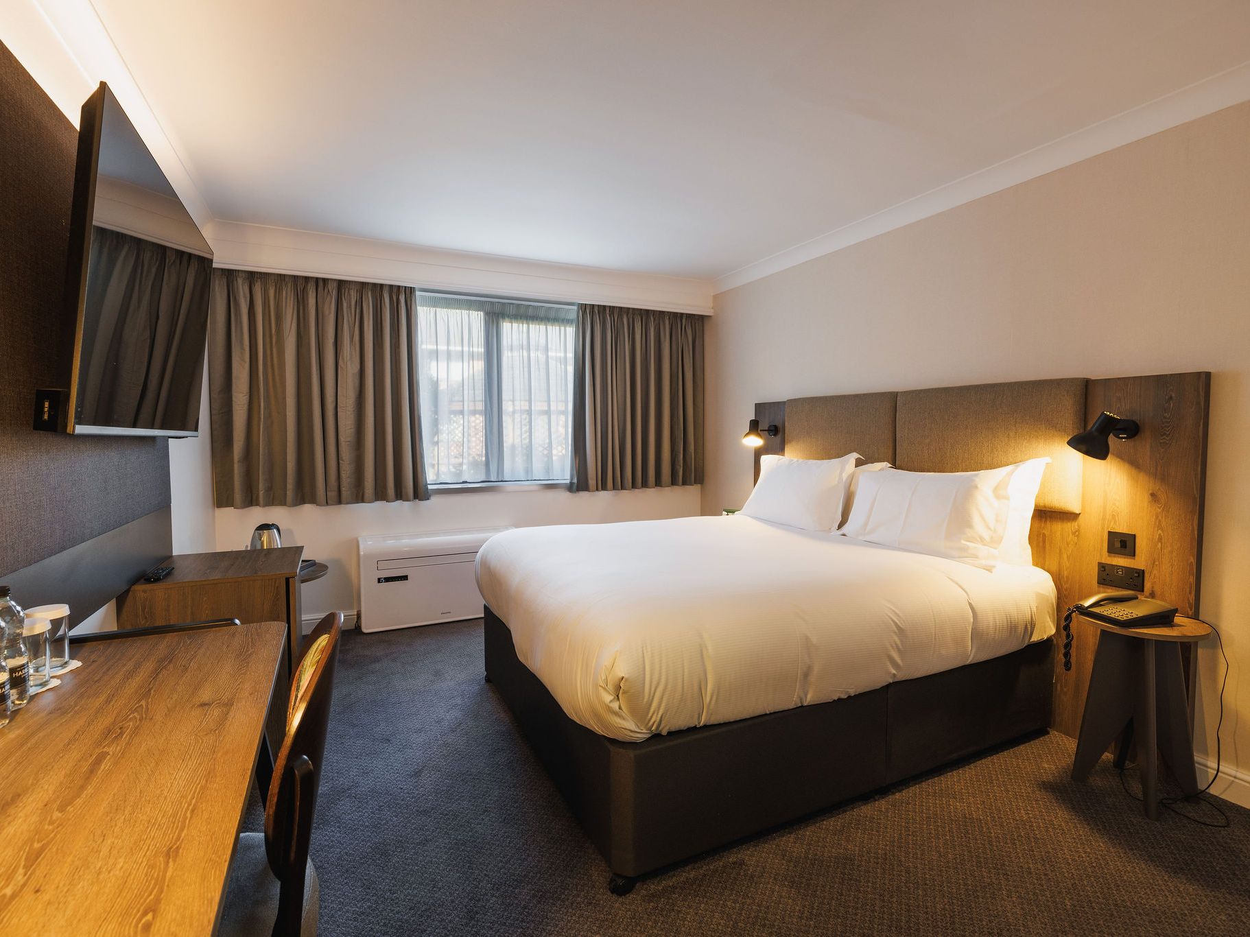 Modern hotel room with a large bed, desk, flat-screen TV, and window with curtains