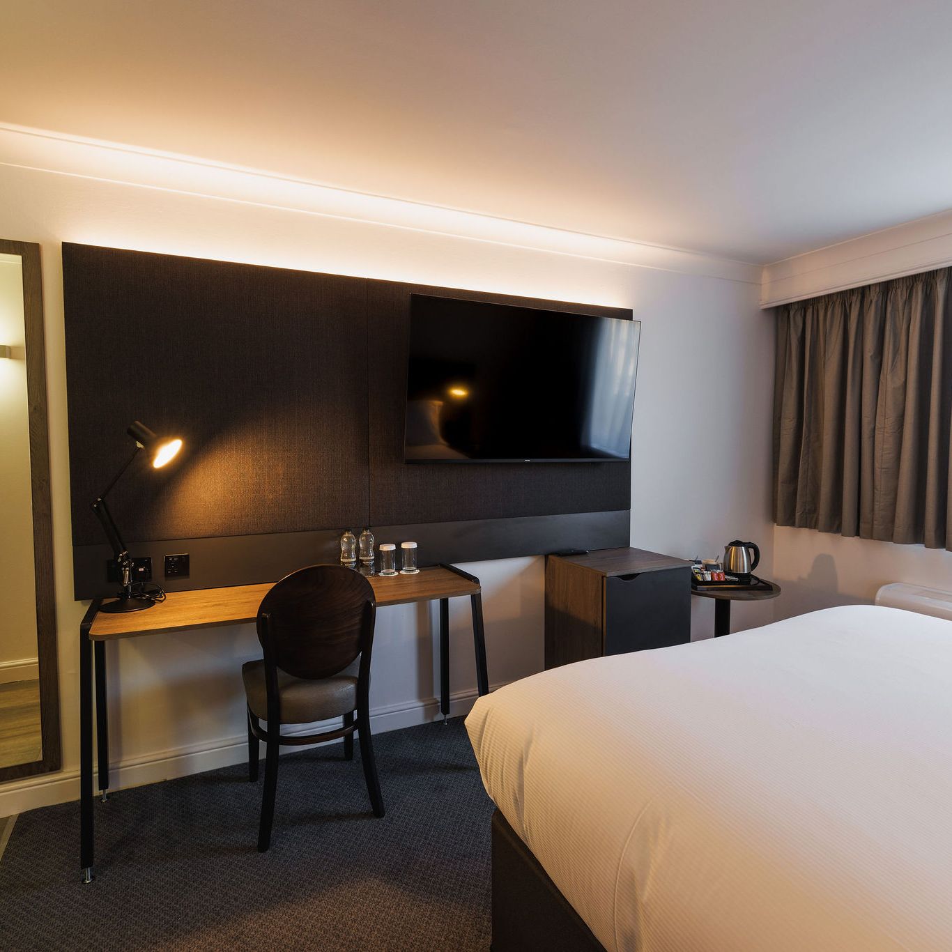 Modern hotel room with desk, TV, bed, and window with curtains