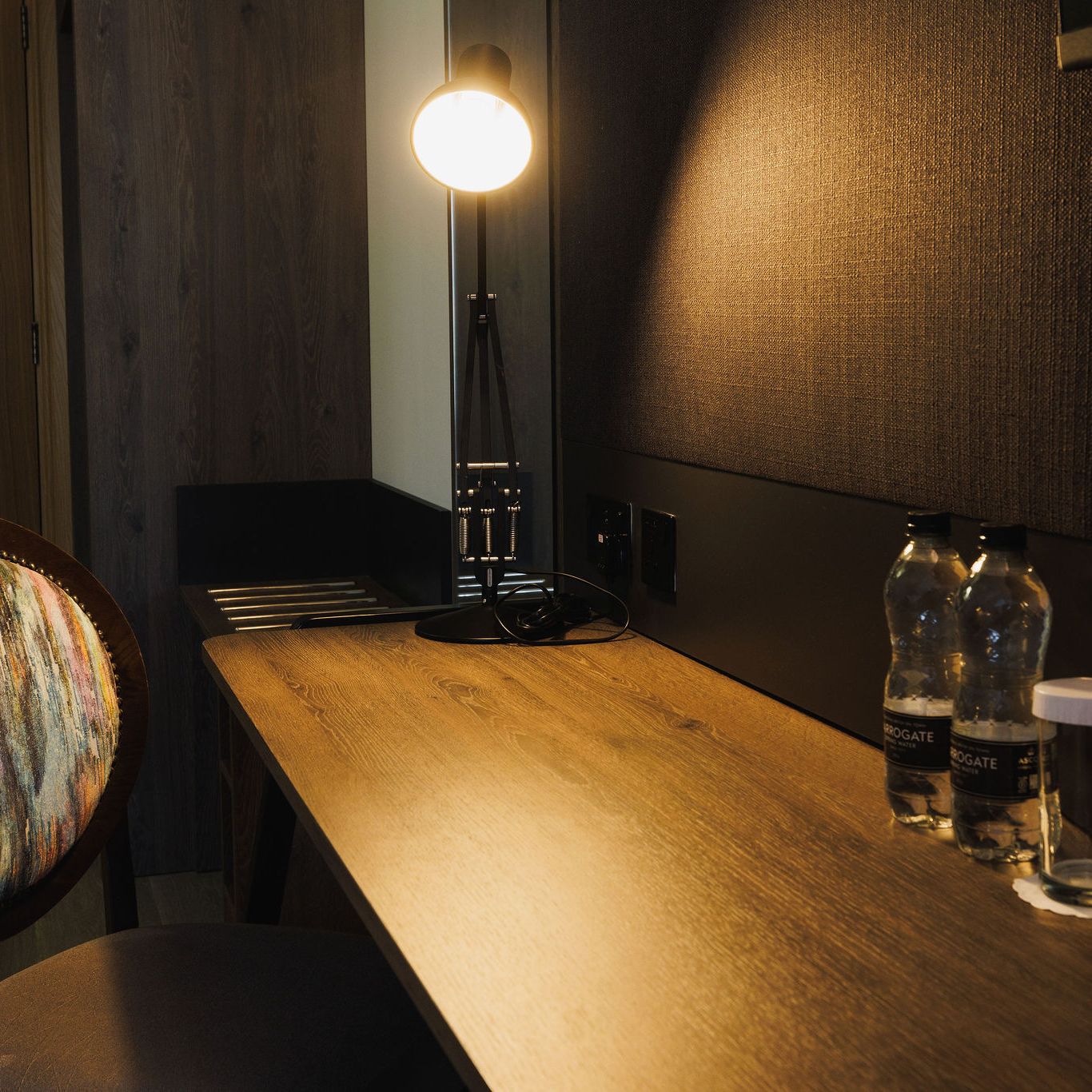 Desk with a lamp, two water bottles, two glasses, and a colorful chair in a hotel room