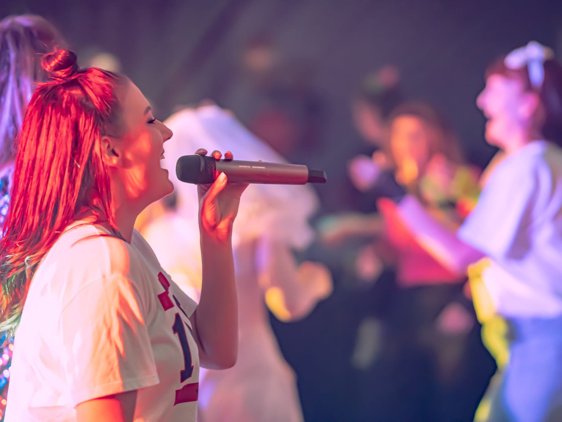 Woman singing into a microphone on stage with colorful lighting and blurred people in the background