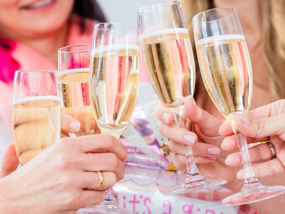 Group of women clinking champagne glasses in celebration with a pink 'It's a Girl!' balloon in the background.