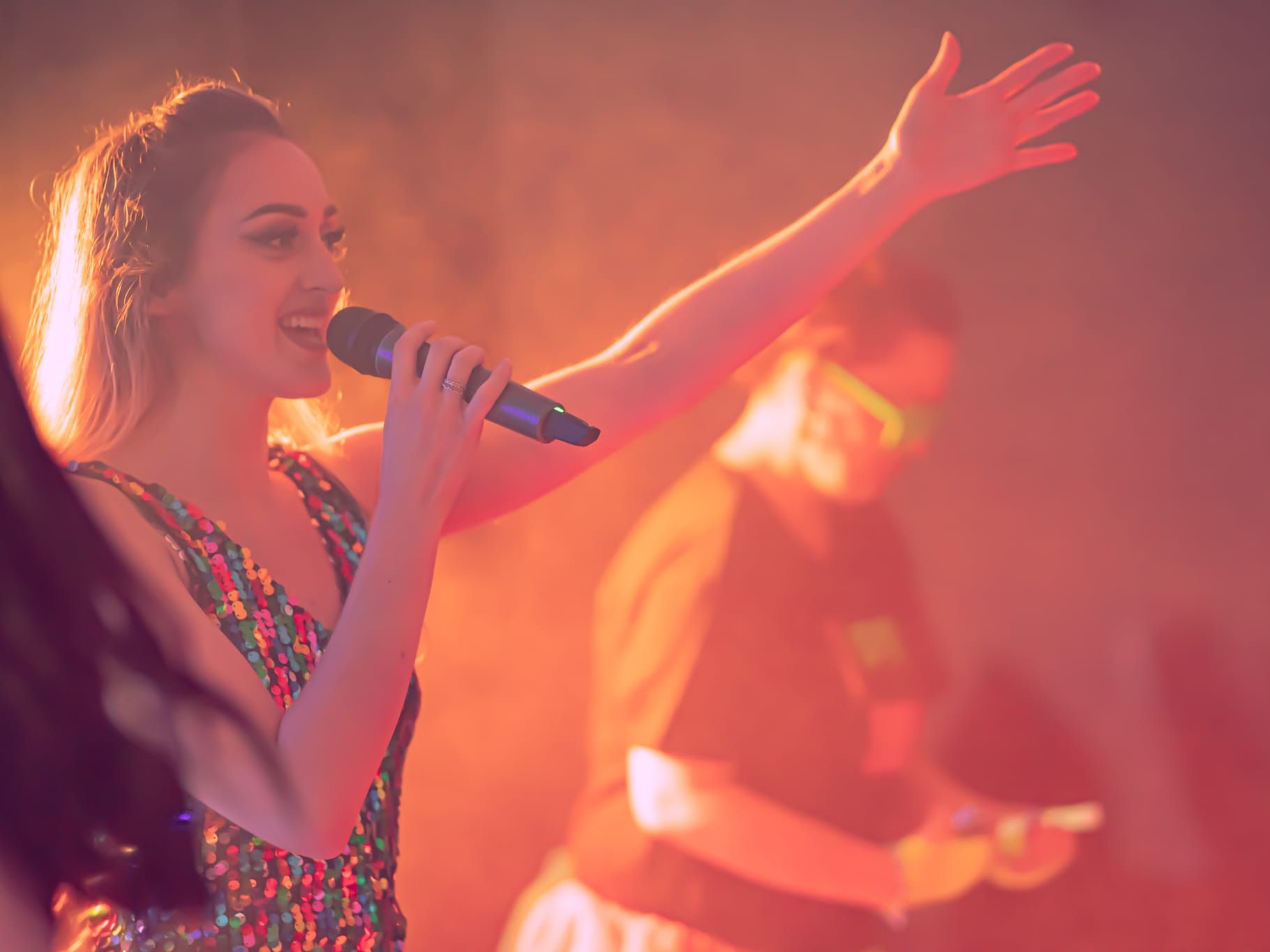 Woman singing on stage with microphone in colorful lighting