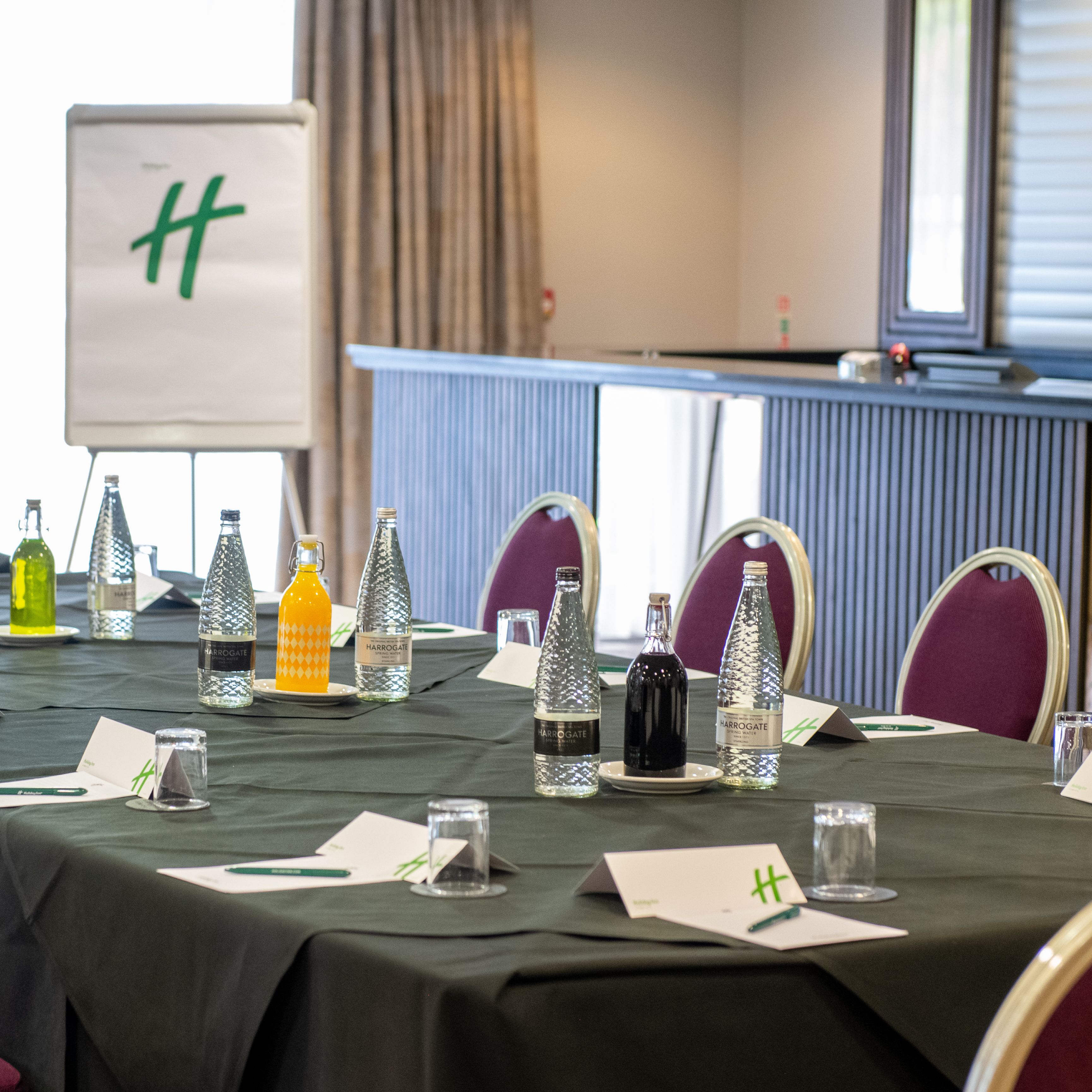 Conference room setup with beverages, notepads, and a flip chart with a green H logo.