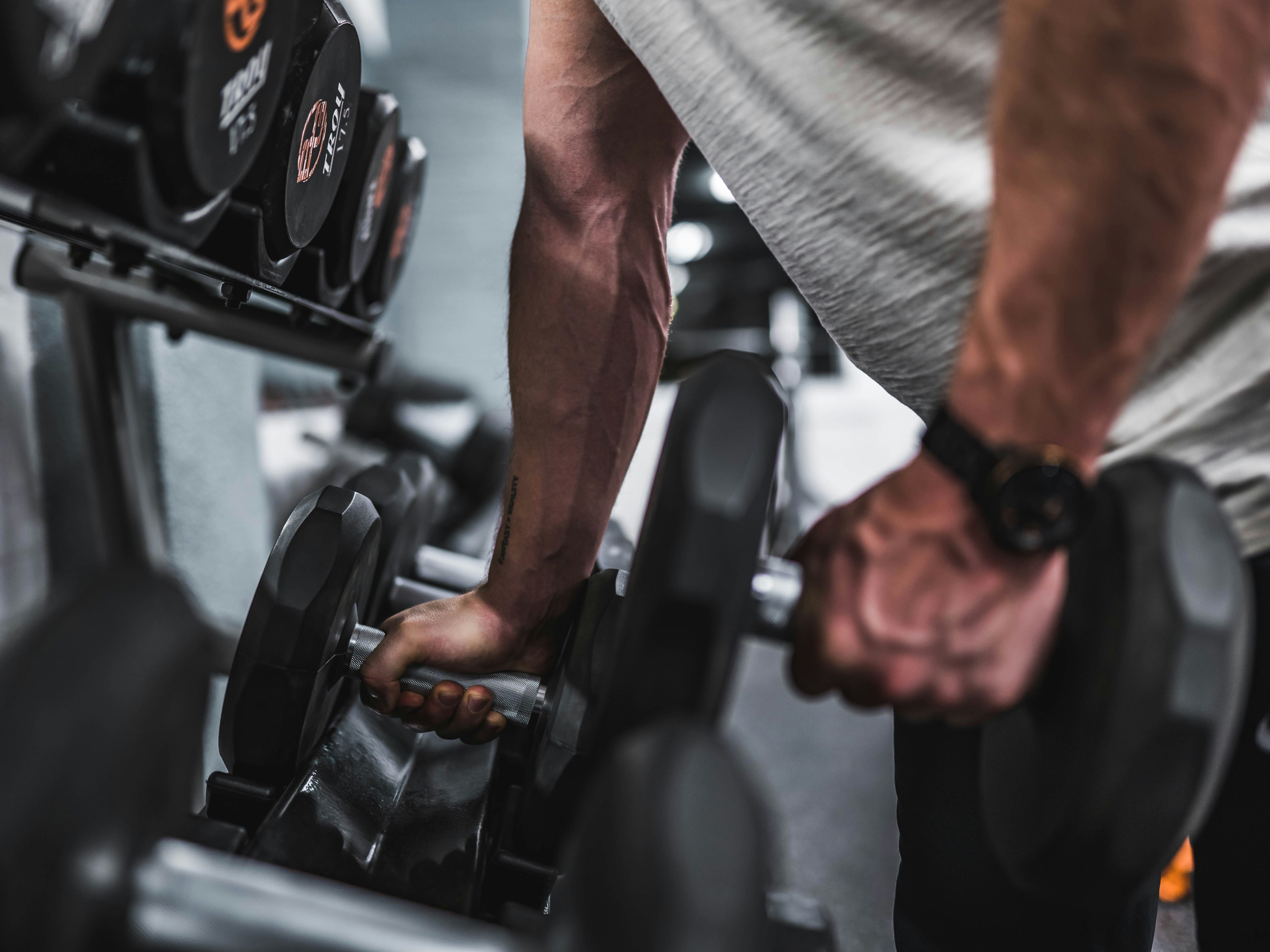 Person picking up dumbbells from a rack in a gym