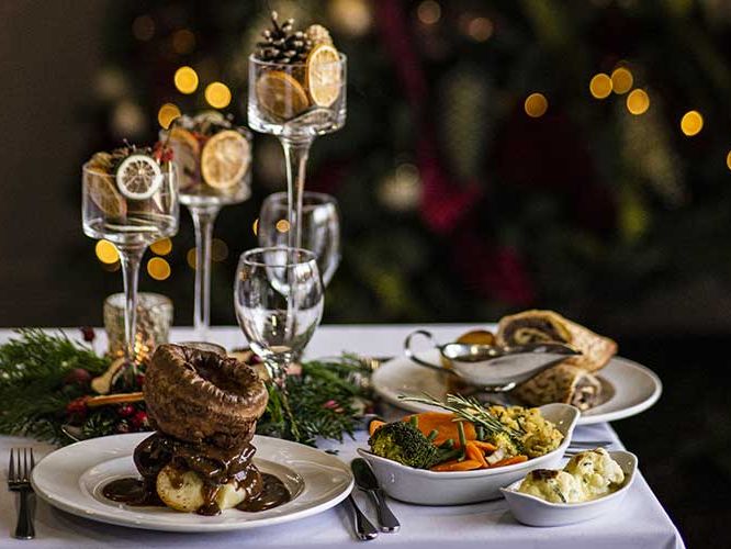 Festive holiday table set with traditional roast dinner, vegetables, and elegant decorations.