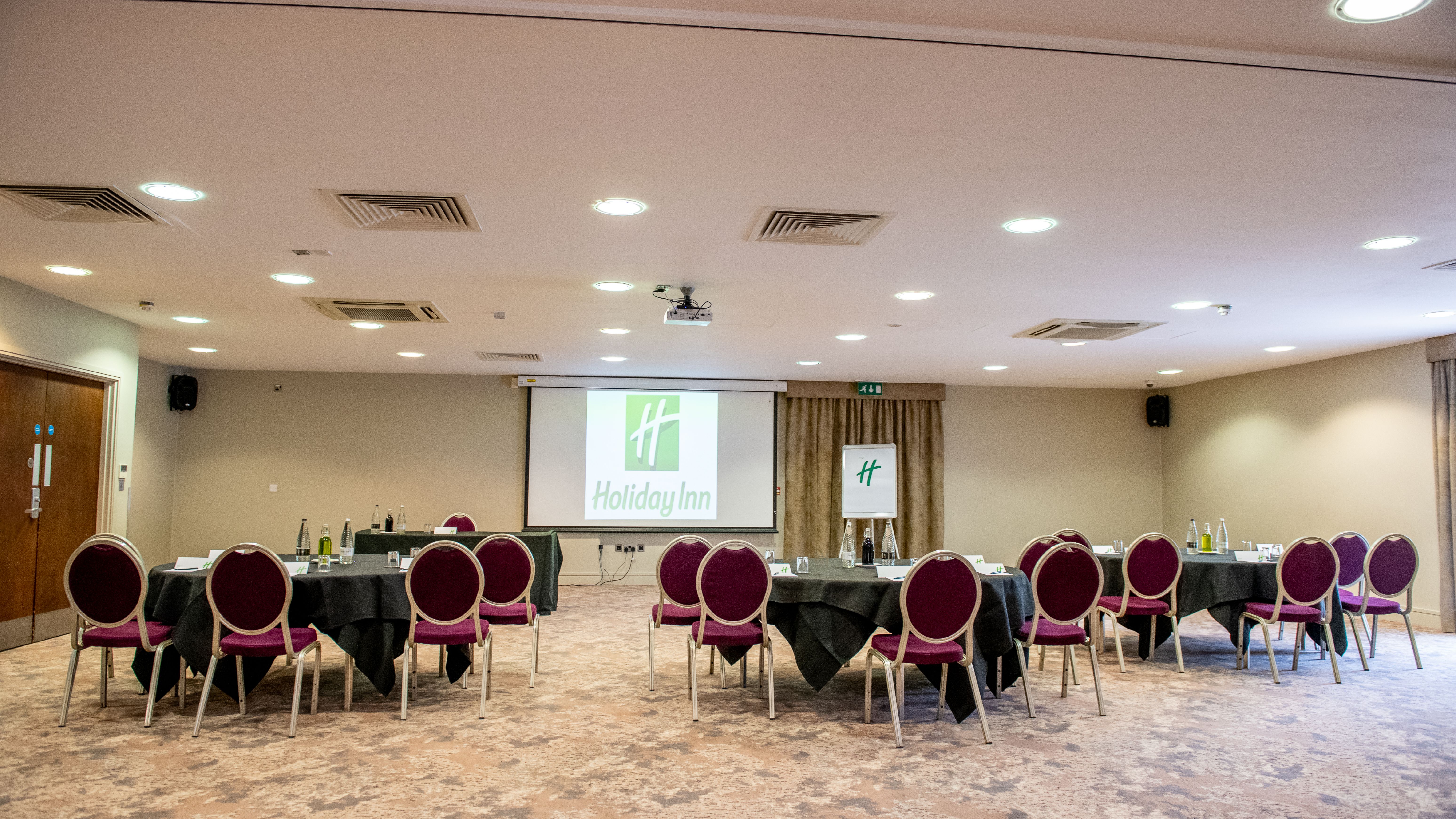 Holiday Inn conference room with round tables and chairs arranged for a meeting.