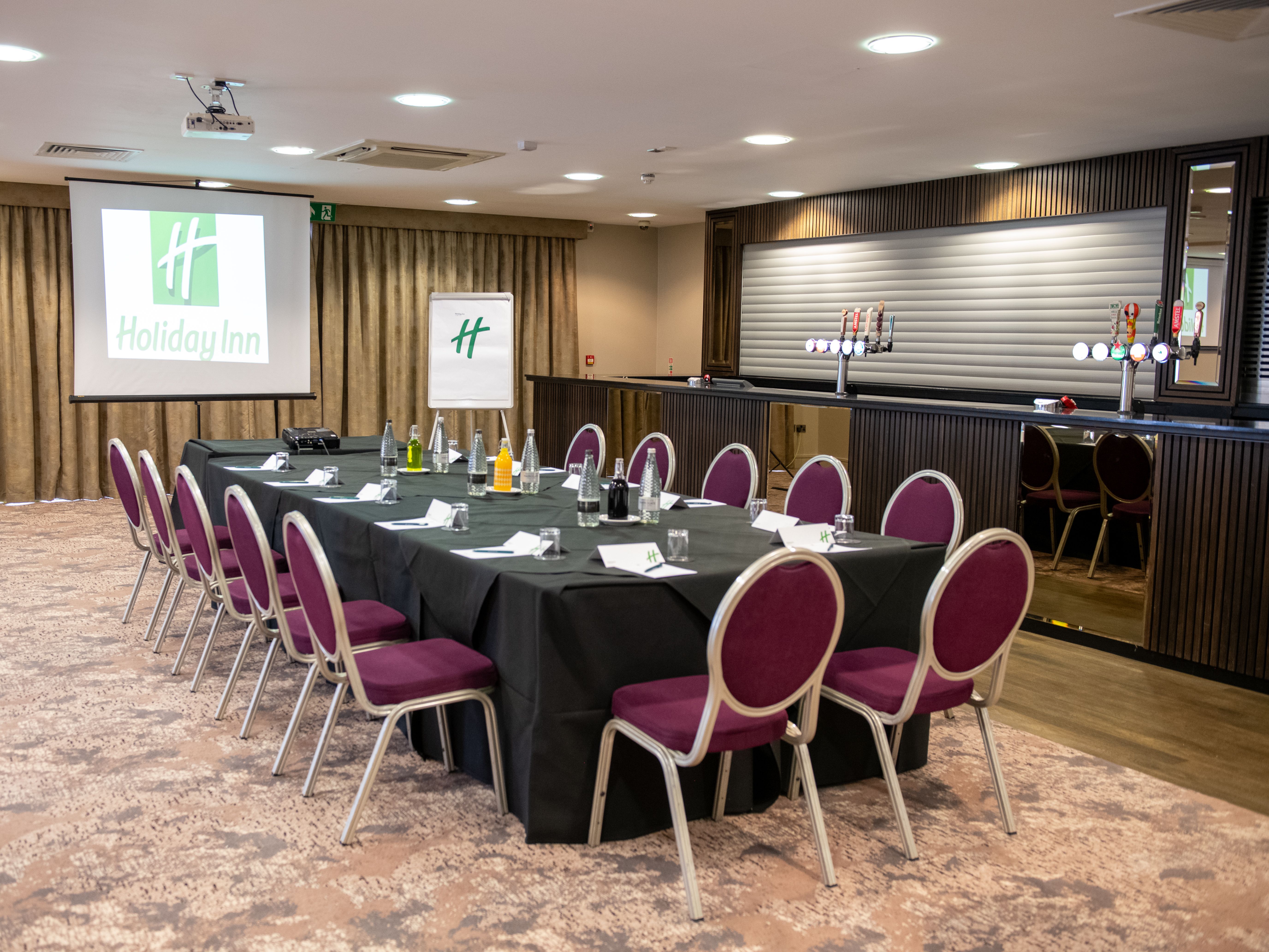 Holiday Inn conference room with table setup, chairs, projector screen, and bar area