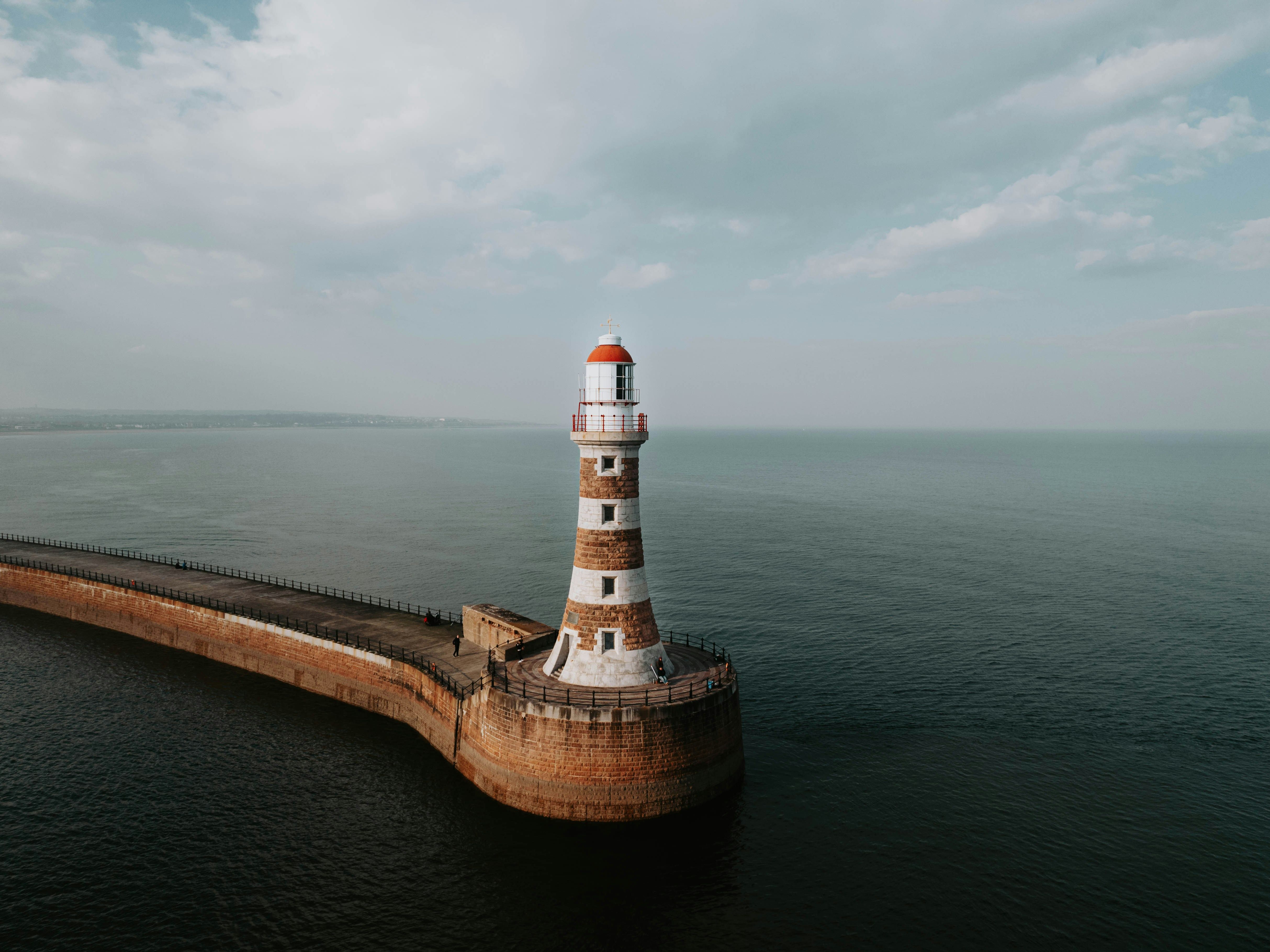 Lighthouse on a pier extending into the calm ocean under a cloudy sky