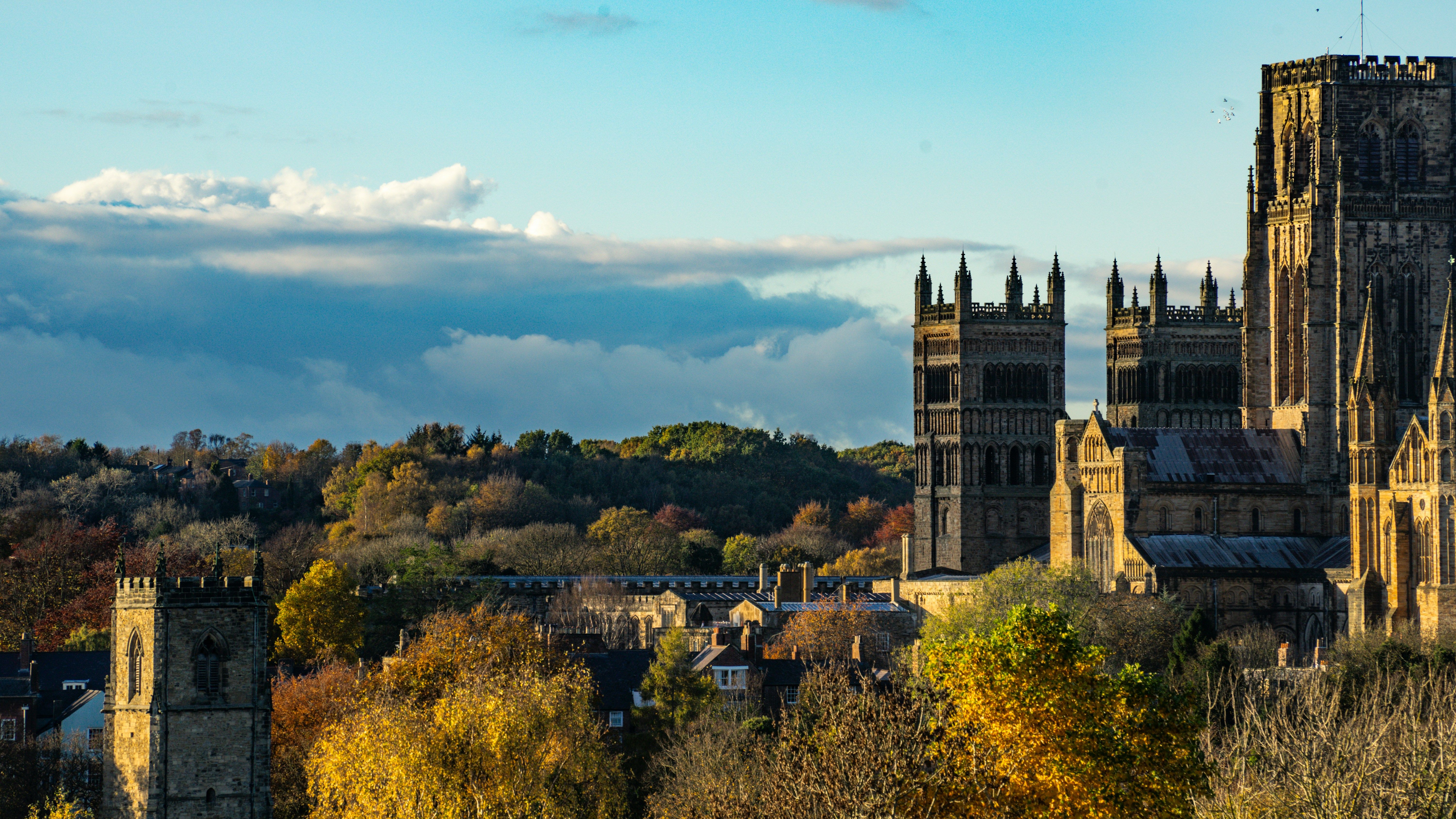 A historic cathedral with tall towers in a scenic autumn landscape under a blue sky with clouds.