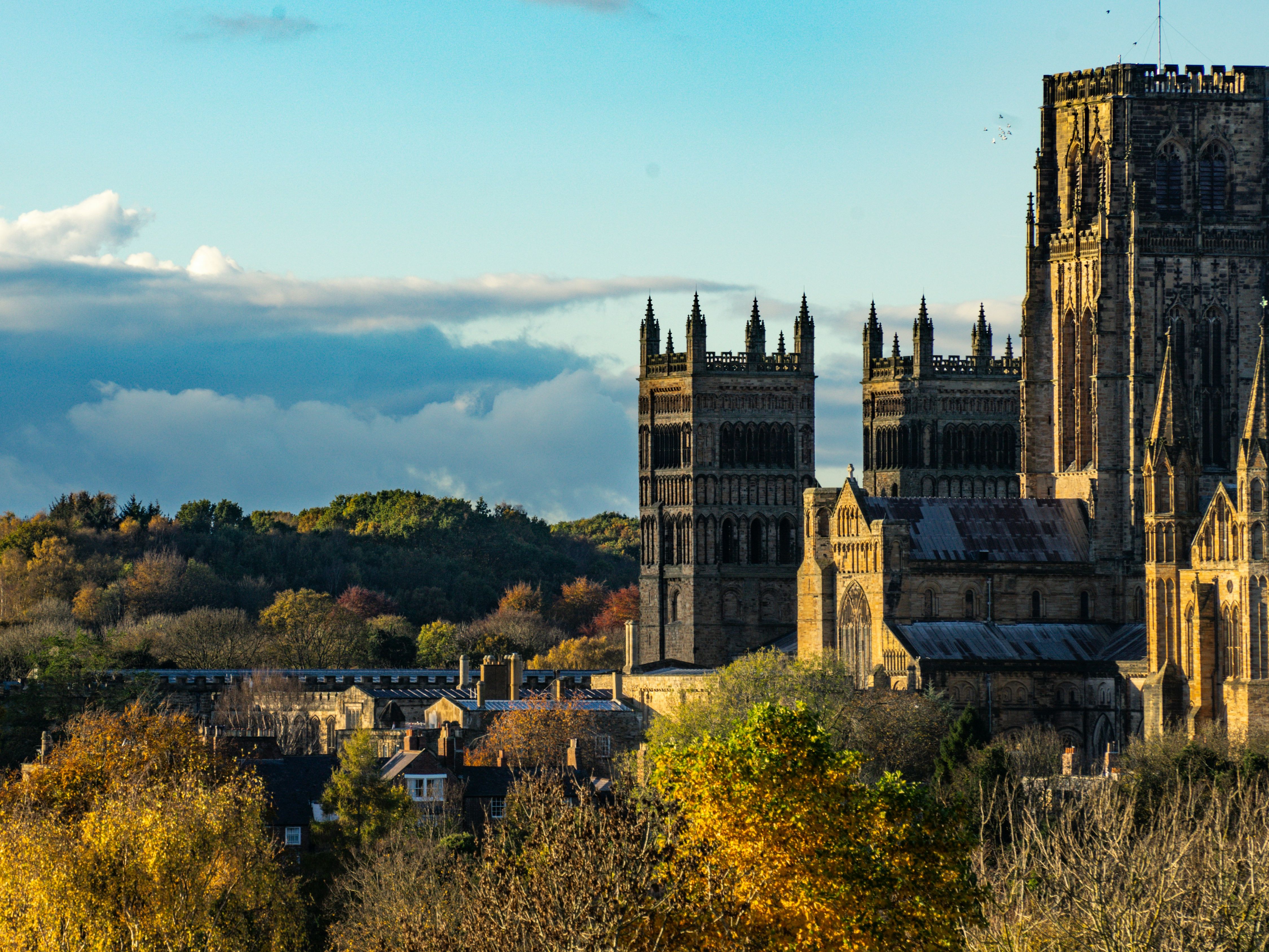 A historic cathedral with tall towers in a scenic autumn landscape under a blue sky with clouds.