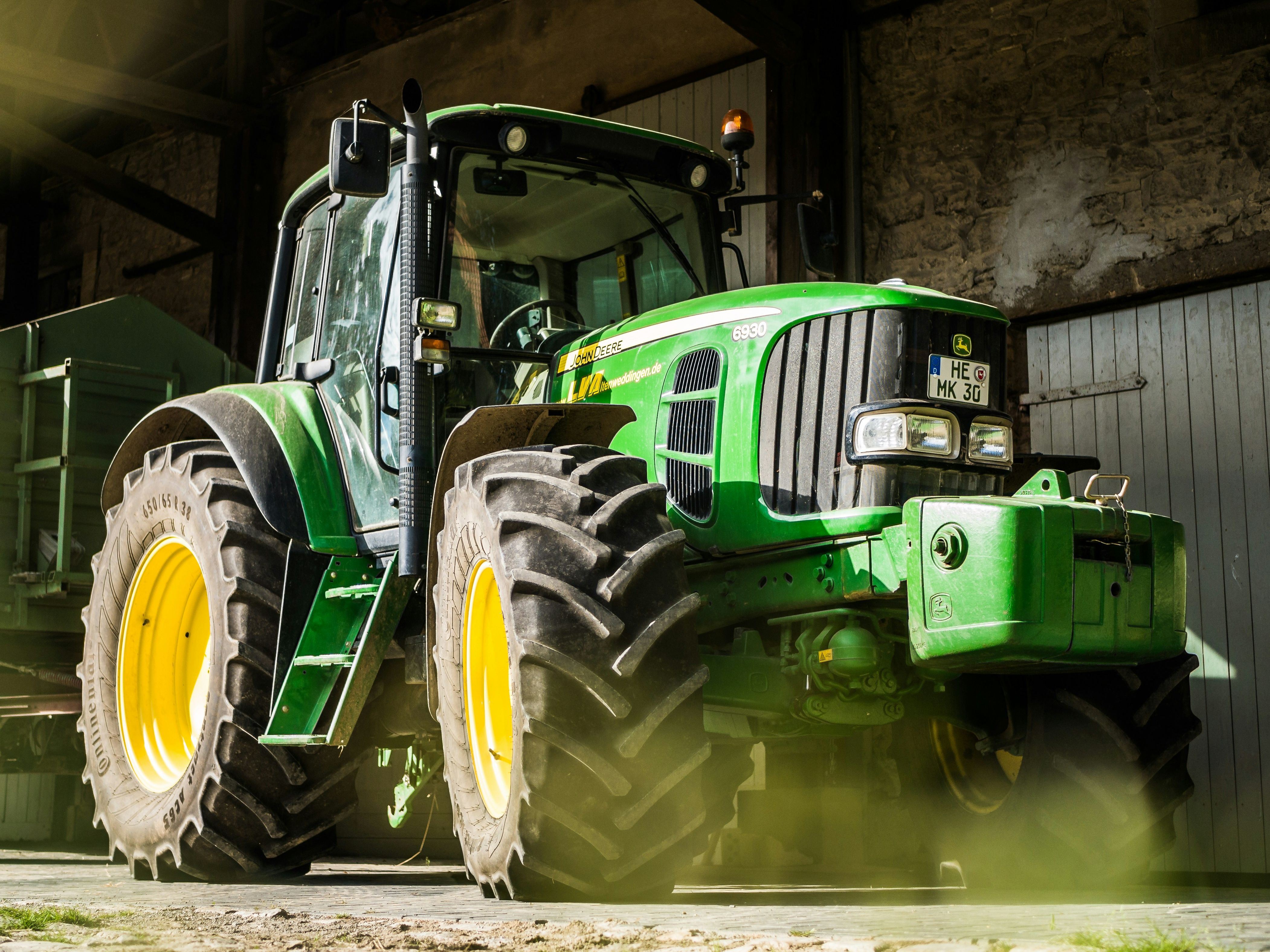 Large green John Deere tractor with yellow wheels parked inside a barn