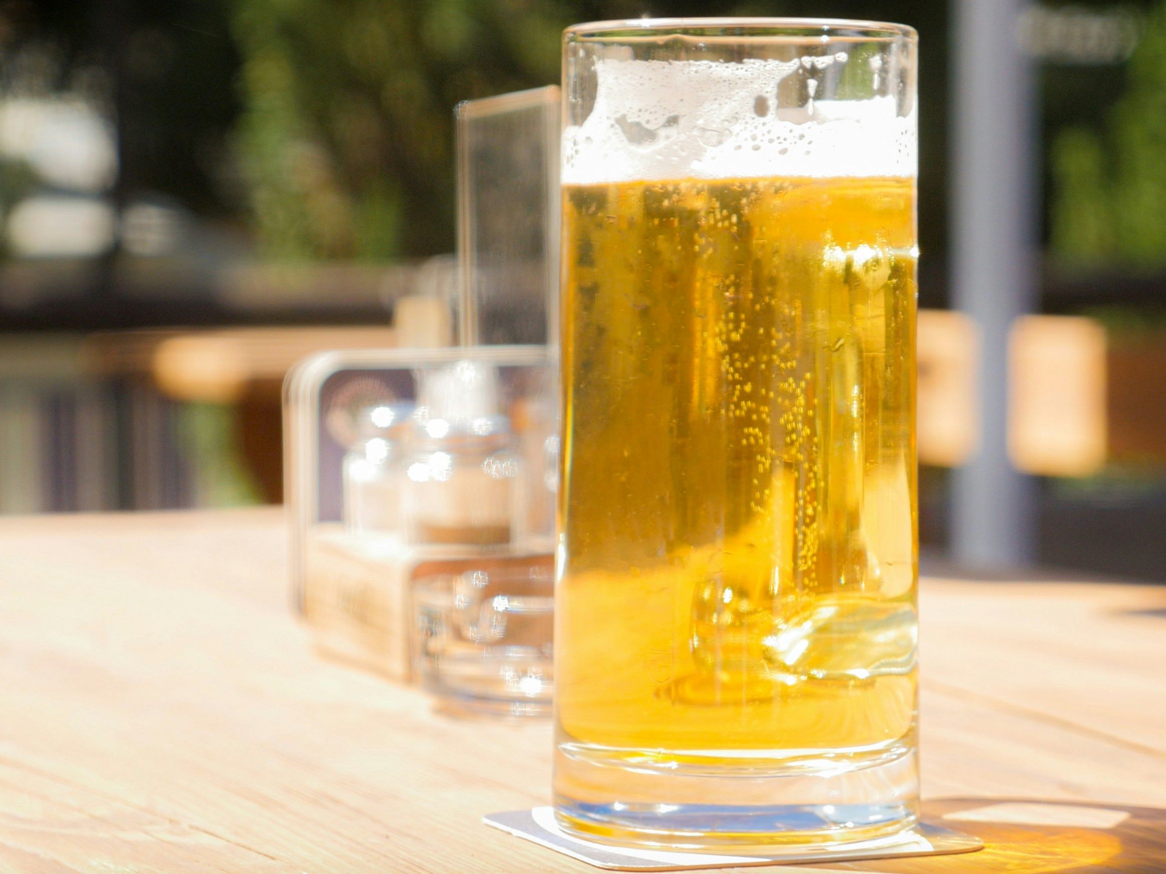 A glass of beer on a wooden outdoor table.
