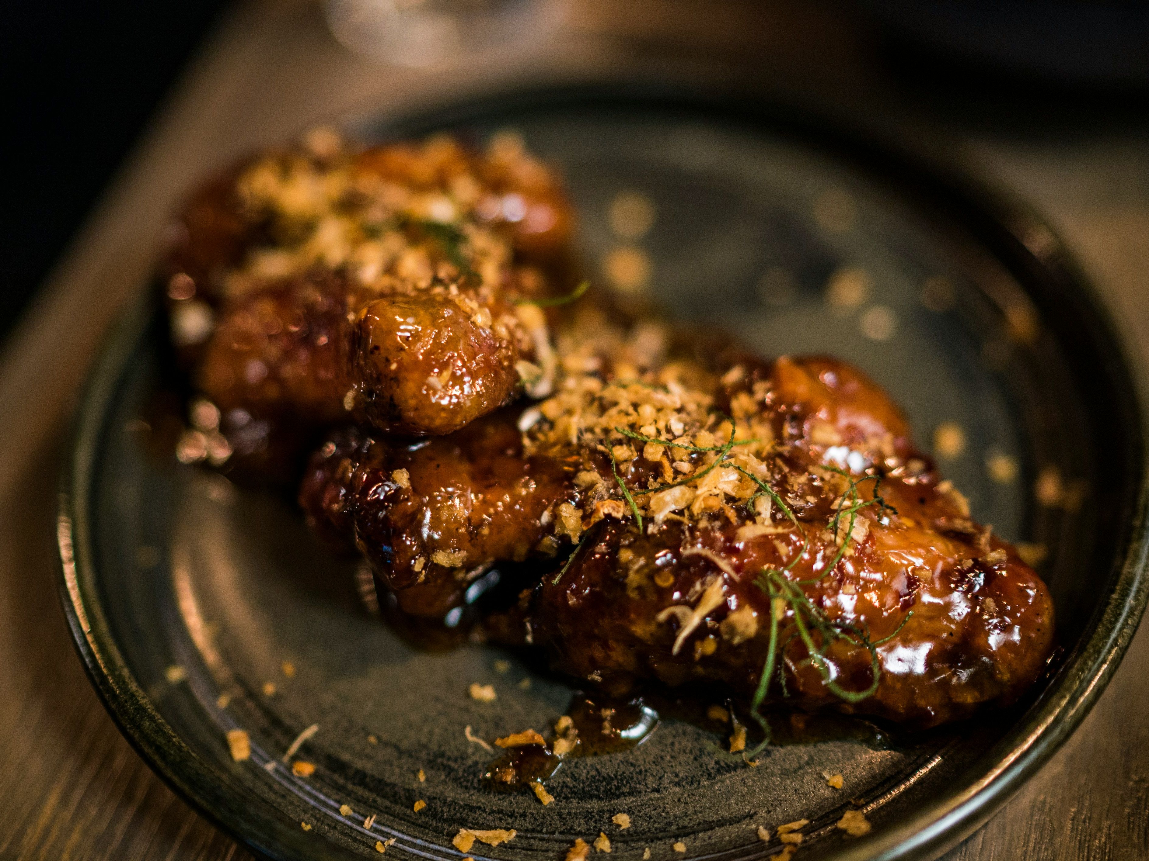 Close-up of glazed chicken wings garnished with herbs and crispy bits on a dark plate