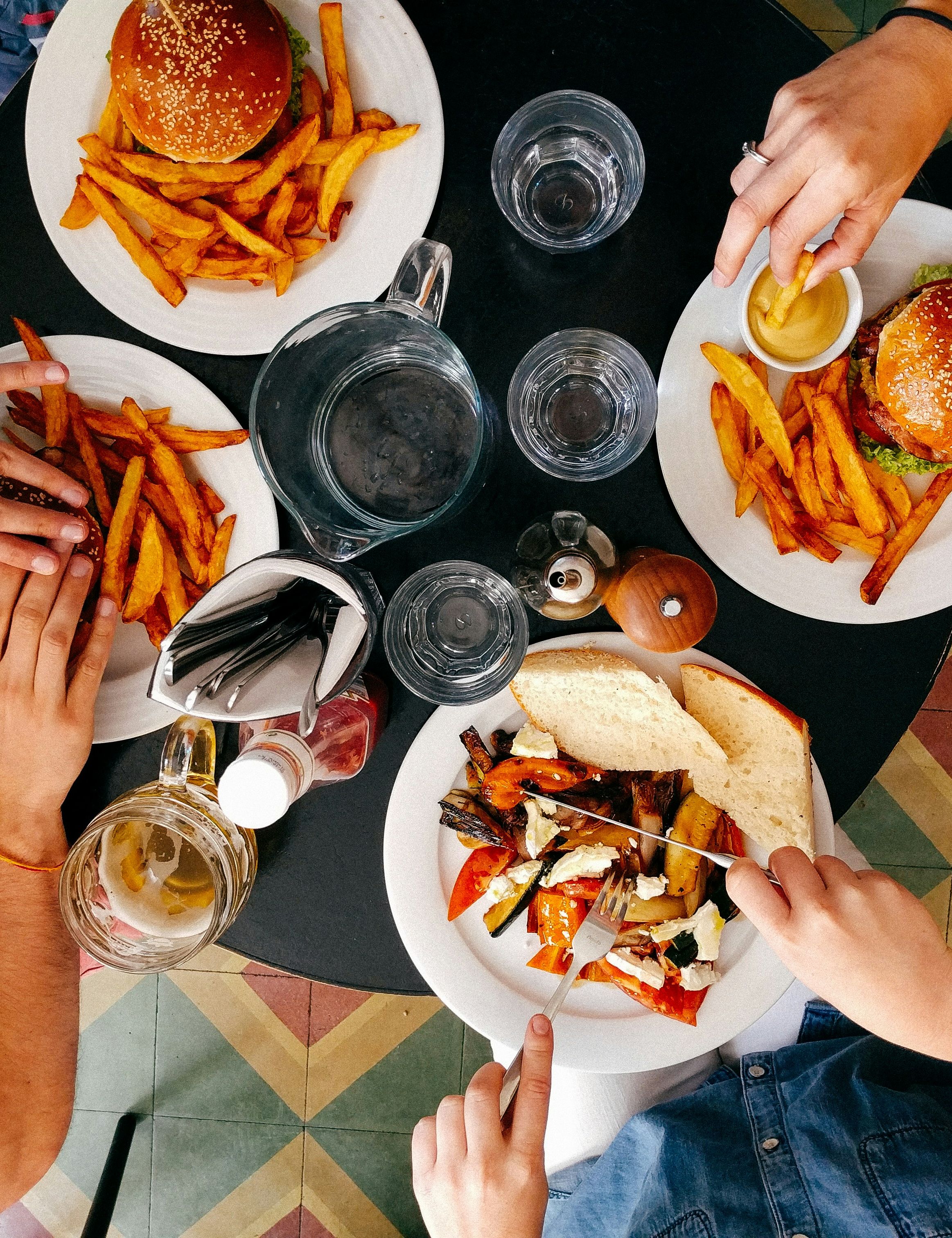 Top-down view of three people eating burgers, fries, and a sandwich at a restaurant table.